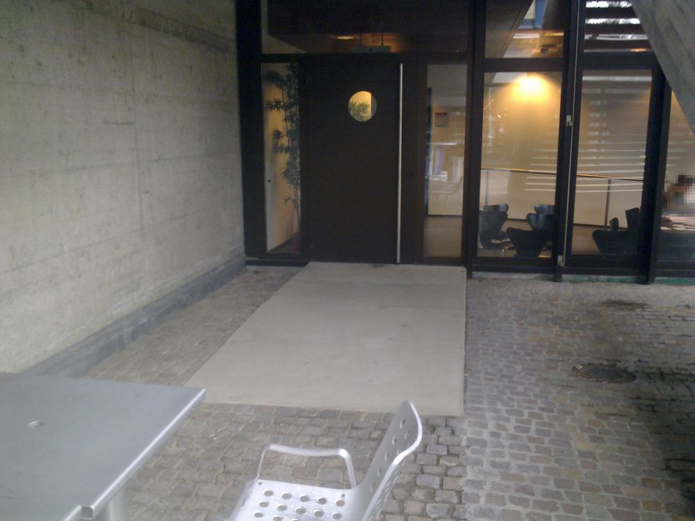 Y05-G, Balkon/Terrasse: Die Türe ins Café von aussen. Vor der Tür existiert eine kurze Beton-Rampe mit einer Neigung von 5%.