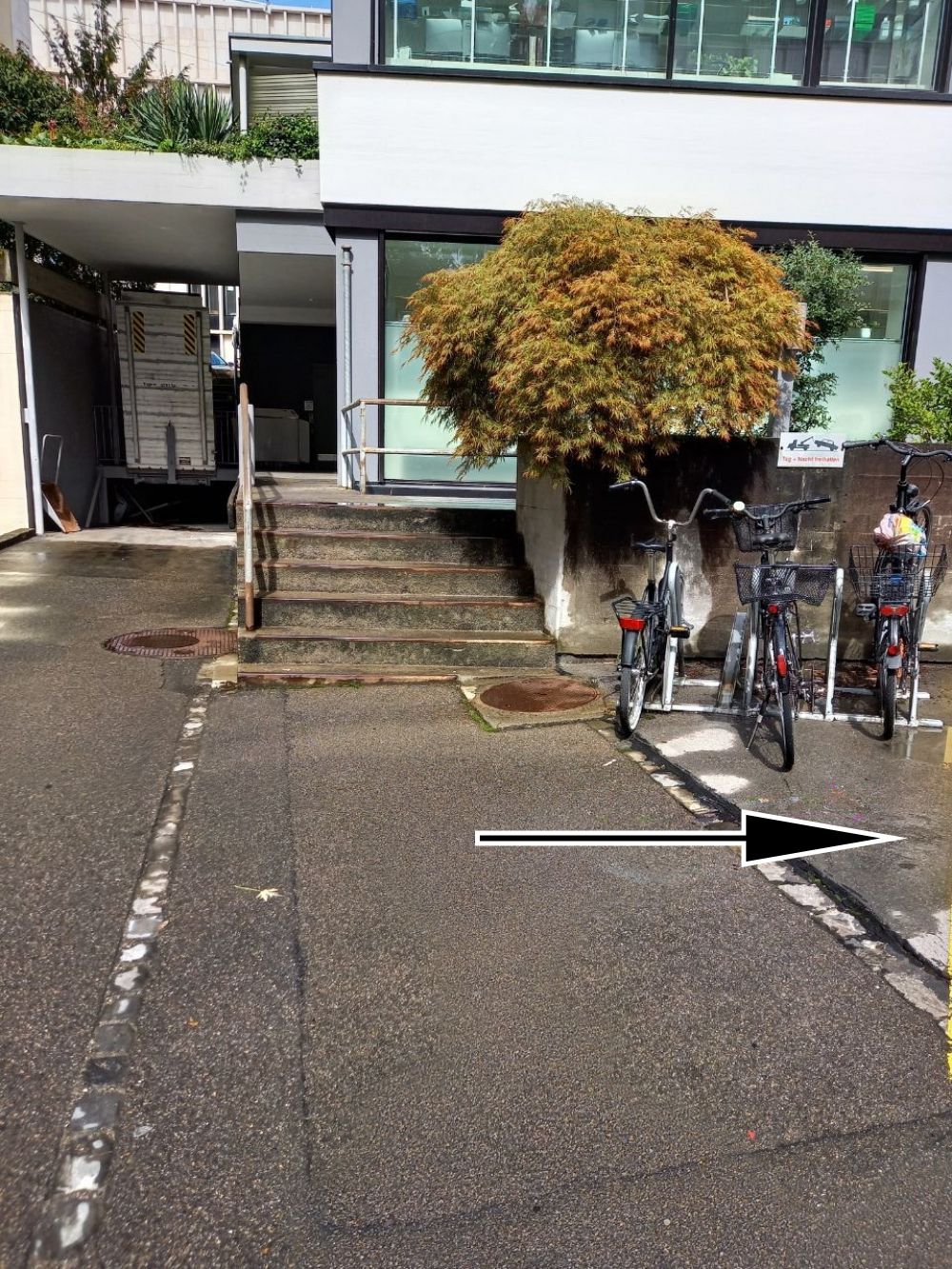 Gebäude RAL: Drei Parkplätze links (mit Pfeil markiert). Geradeaus befindet sich der Eingang ins 1UG./ Stockwerk D. Dieser Eingang ist nur von der anderen Seite des Gebäudes stufenlos zugänglich.