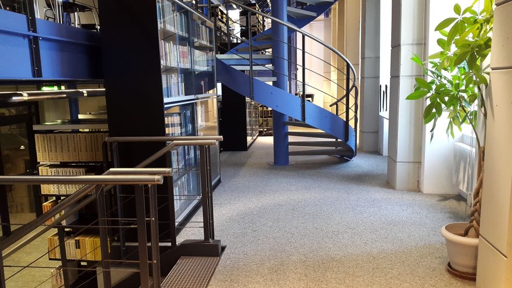 Leseplatz-Raum ZUB-E-7: Sicht von der rechten vorderen Seite des Zwischenstockwerkes aus auf die Wendeltreppe in der Mitte des Stockwerkes, welche ins 1. und 2. Obergeschoss führt, und auf die beiden Treppen links, welche zum Erdgeschoss führen.