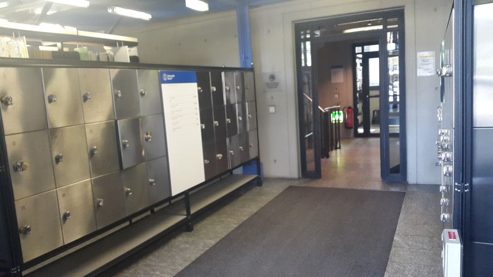 ZUB, Stockwerk E: Sicht vom Haupteingang des Gebäudes aus auf den Flur und Eingangsbereich. Im Flur direkt nach dem Haupteingang befinden sich auf der linken und rechten Seite Schliessfächer mit Vorhängeschloss. Die Schlüssel können in der Biblothek im 2. Obergeschoss bezogen und ausgeliehen werden.