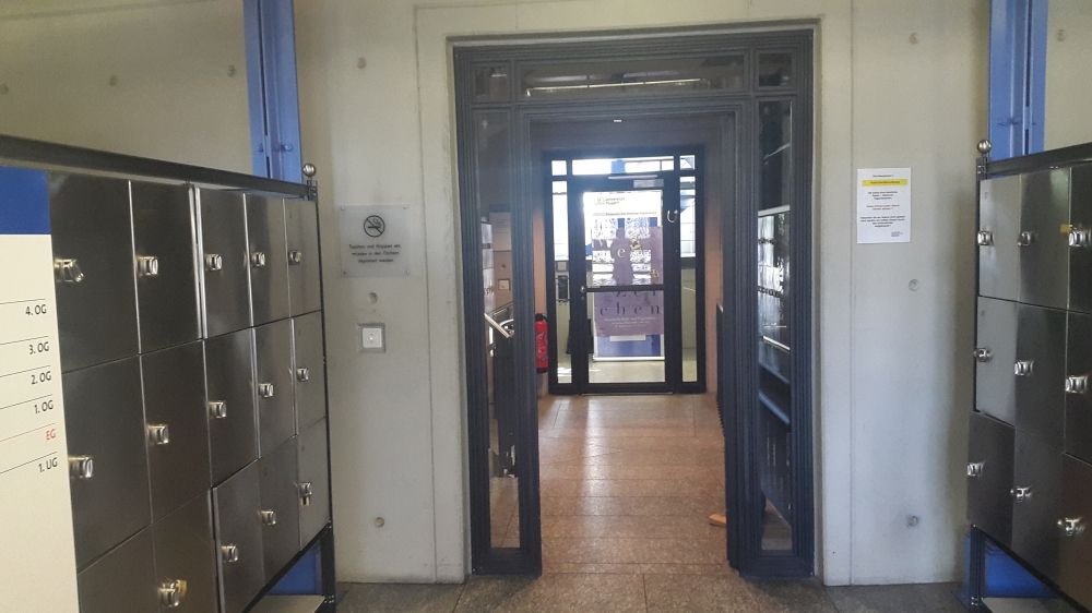 ZUB-E, Bibliothek: Sicht vom Haupteingang aus in Richtung Notfall- und geschlossene Eingangstür zur Bibliothek im Erdgeschoss. Für diesen stufenlosen Zugang zur Bibliothek im Erdgeschoss kann ein Schlüssel im 2. Obergeschoss in der Bibliothek verlangt werden.
Im Gang von Haupteingang aus befinden sich Schliessfächer mit Vorhängeschloss, deren Schlüssel im 2. Obergeschoss der Bibliothek bezogen und ausgeliehen werden können.