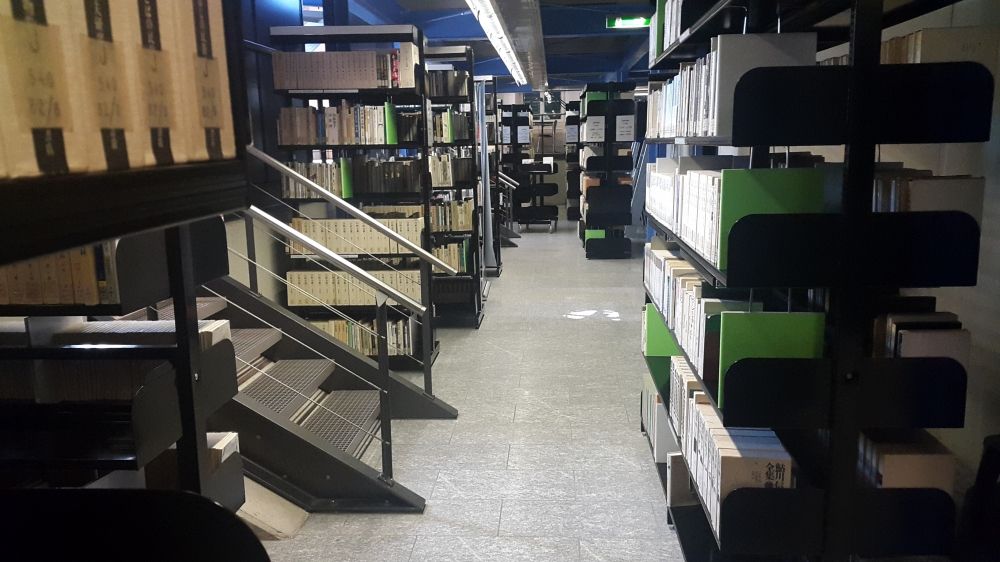 ZUB-E, Bibliothek: Sicht von der linken Seite der Bibliothek im Erdgeschoss aus auf den Eingang rechts und auf zwei Treppen links, die zum Zwischenstockwerk führen, welches nicht stufenlos erreicht werden kann.