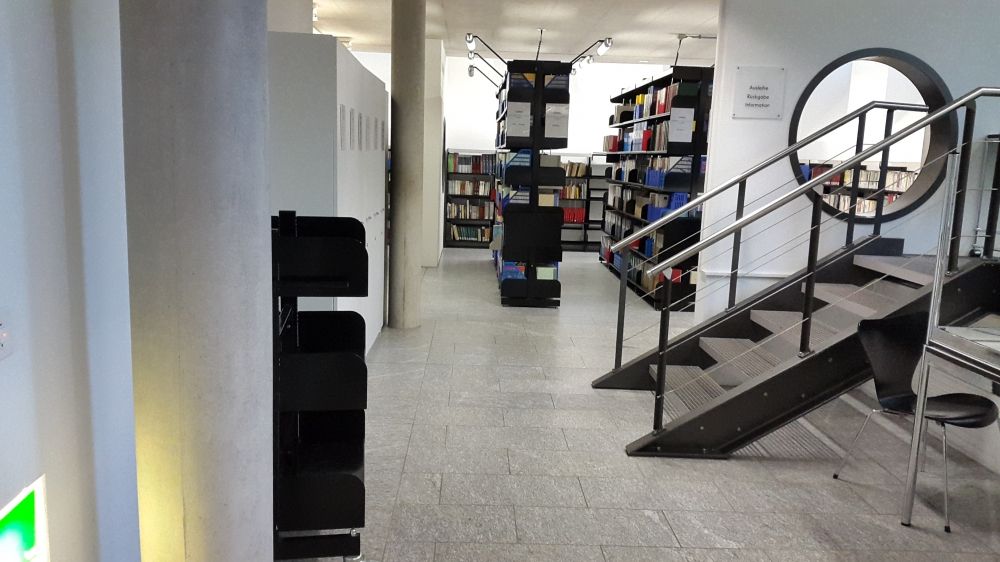 ZUB-U, Bibliothek: Blick vom Eingang aus auf die linke Seite des Raumes. Die Treppe führt zu Büros des Instituts.