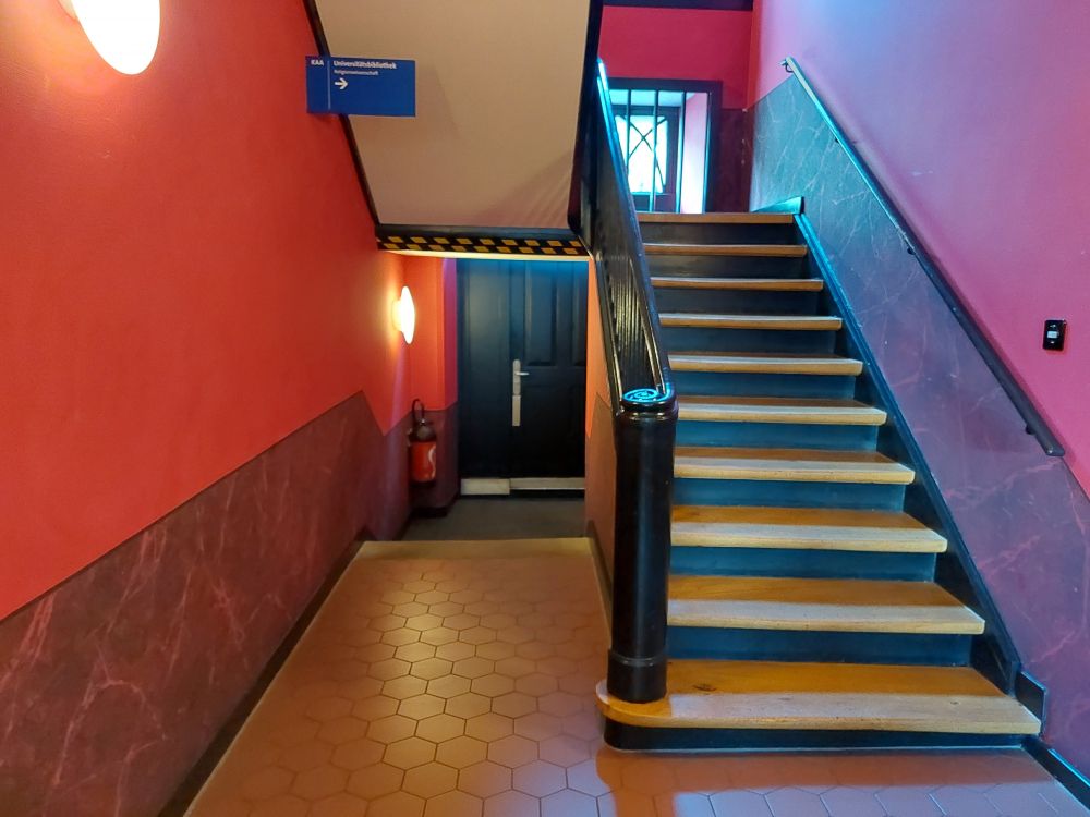 KAA-D, Bibliothek: Eingang, links 2 Treppenstufen ohne Handlauf, Zugang zur Treppe.