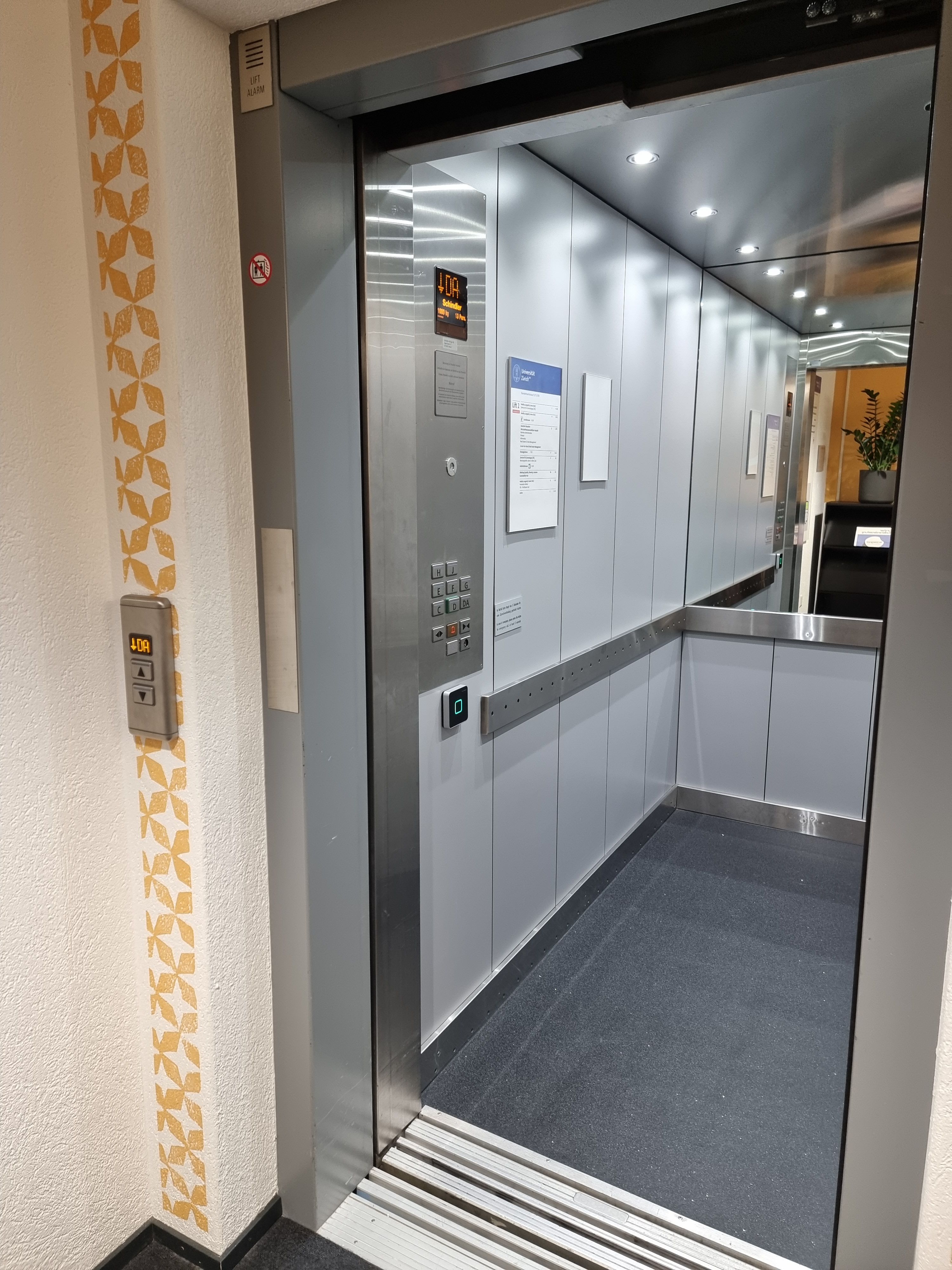 Da 926: Foto vom Lift von Aussen. Die Tür vom Lift ist offen. Die Tasten für den Lift sind auf der linken Seite. Die Liftwand gegenüber des Lifteingangs ist verspiegelt. Das Foto wurde auf dem Stockwerk Da geschossen.