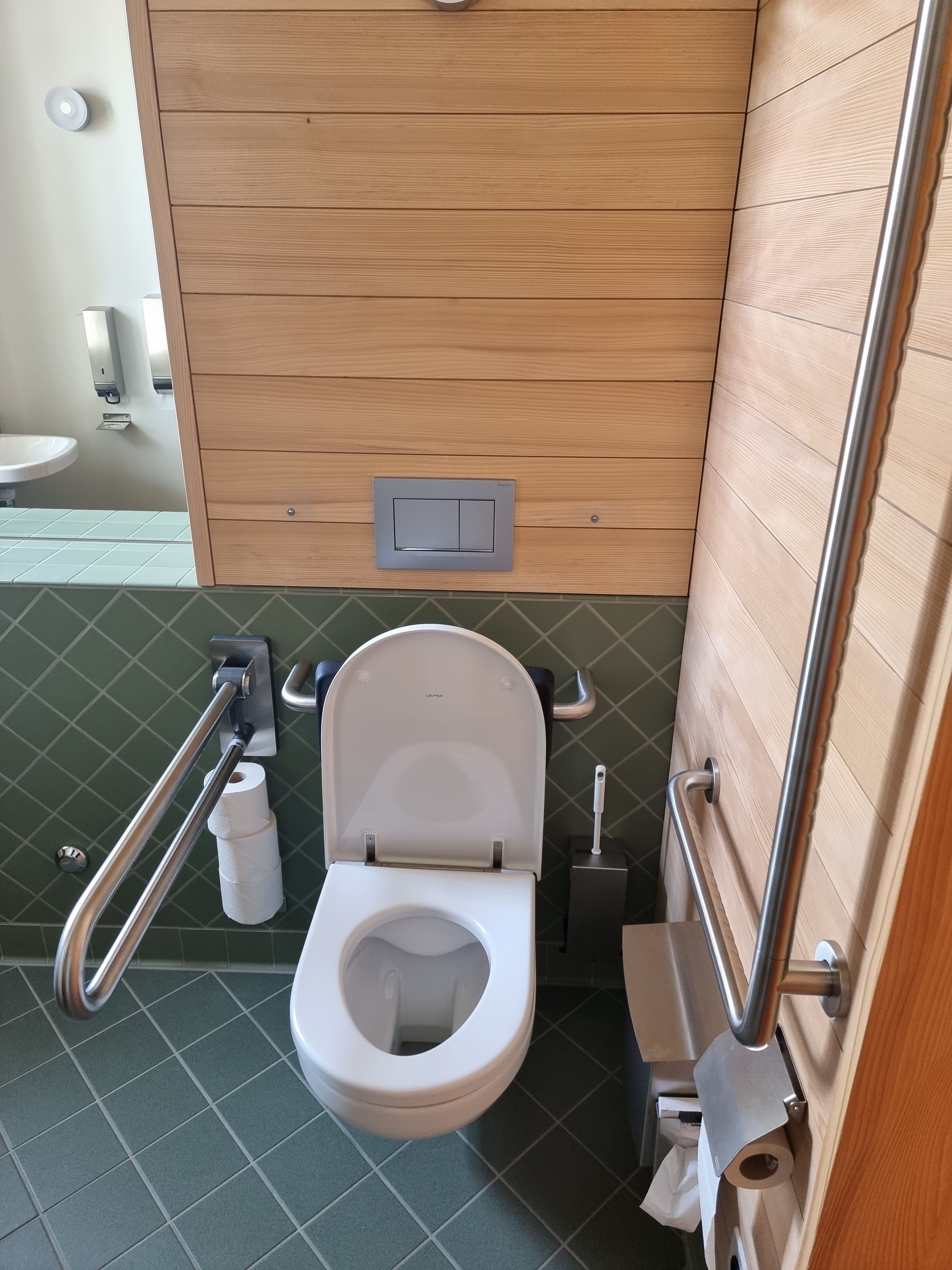 E-108: Bild des Rollstuhl-WCs von vorne. Der Hebel an der Seite ist runtergeklappt.