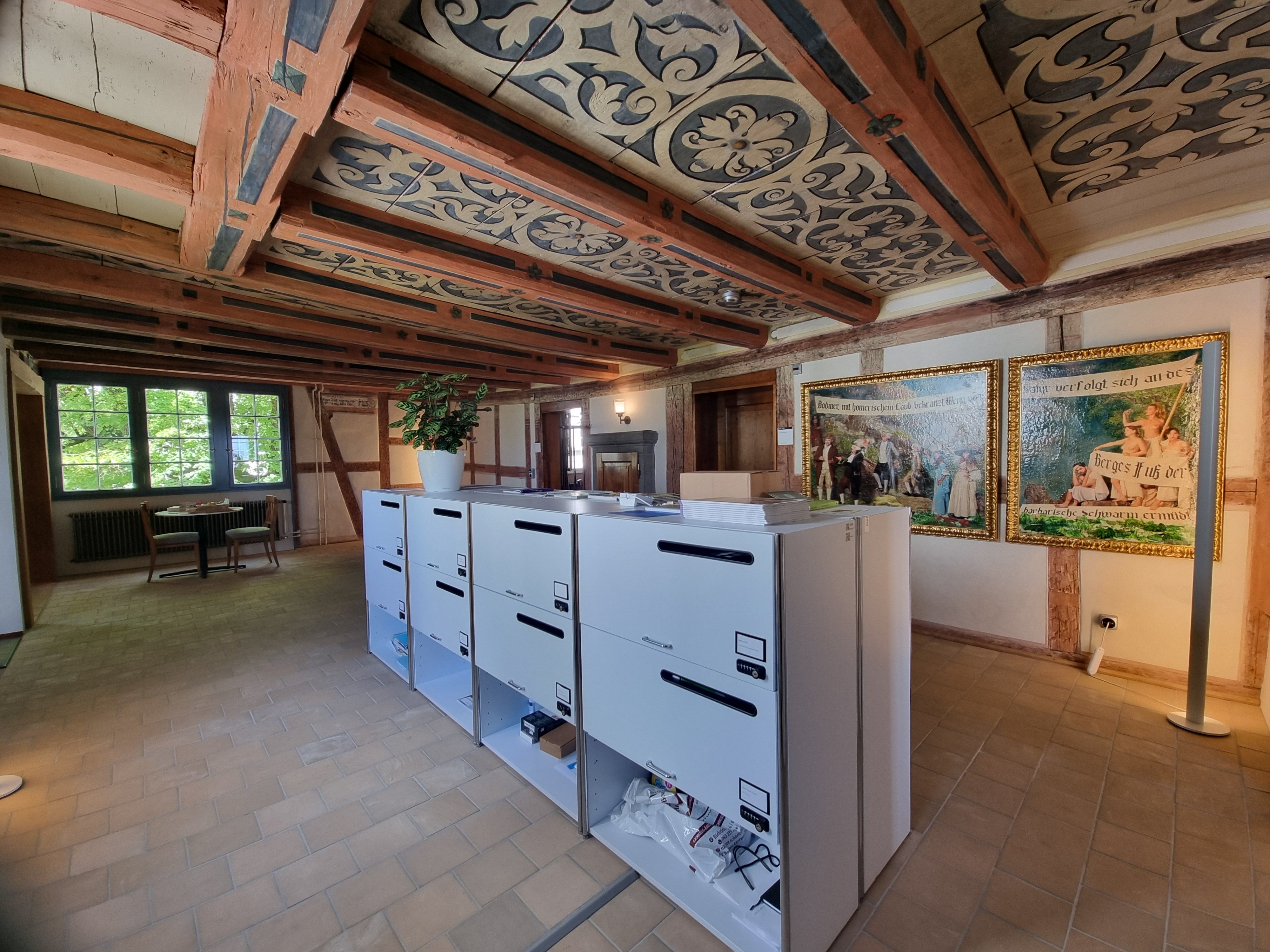 SOB 1. Stock: Bild des Vorraums vom Stockwerk. In der Mitte des Vorraums sind mehrere Bürokommoden. Auf der gegenüberliegenden Seite sieht man zwei Gemälde und zwei Bürotüren.