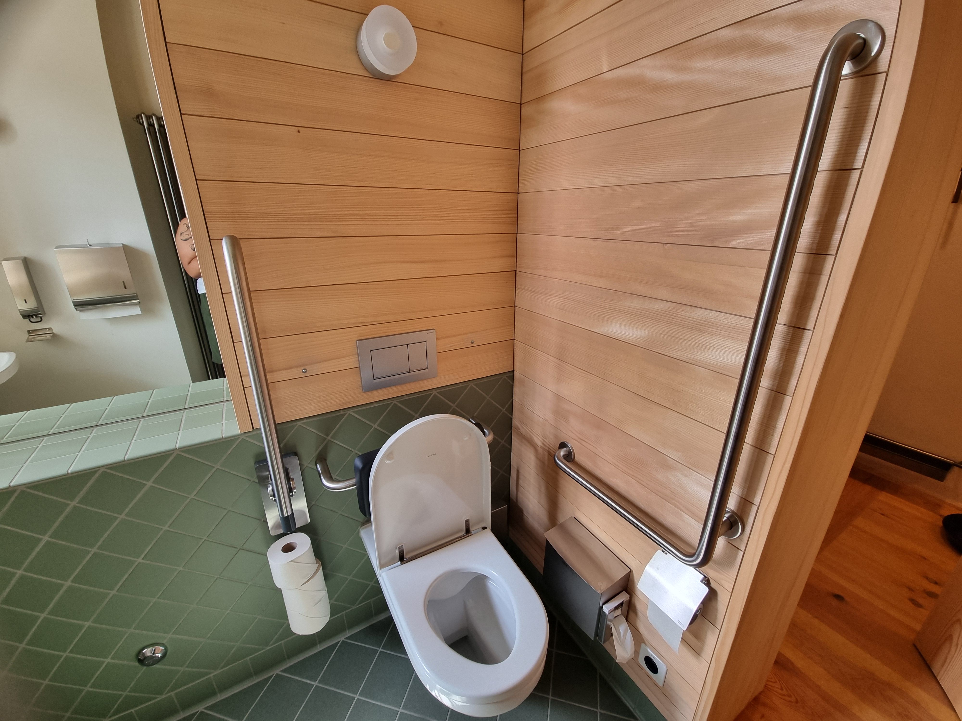 E-108: Seitliches Bild des Rollstuhl-WCs. Der Bügel an der Seite lässt sich hoch- und runterklappen.