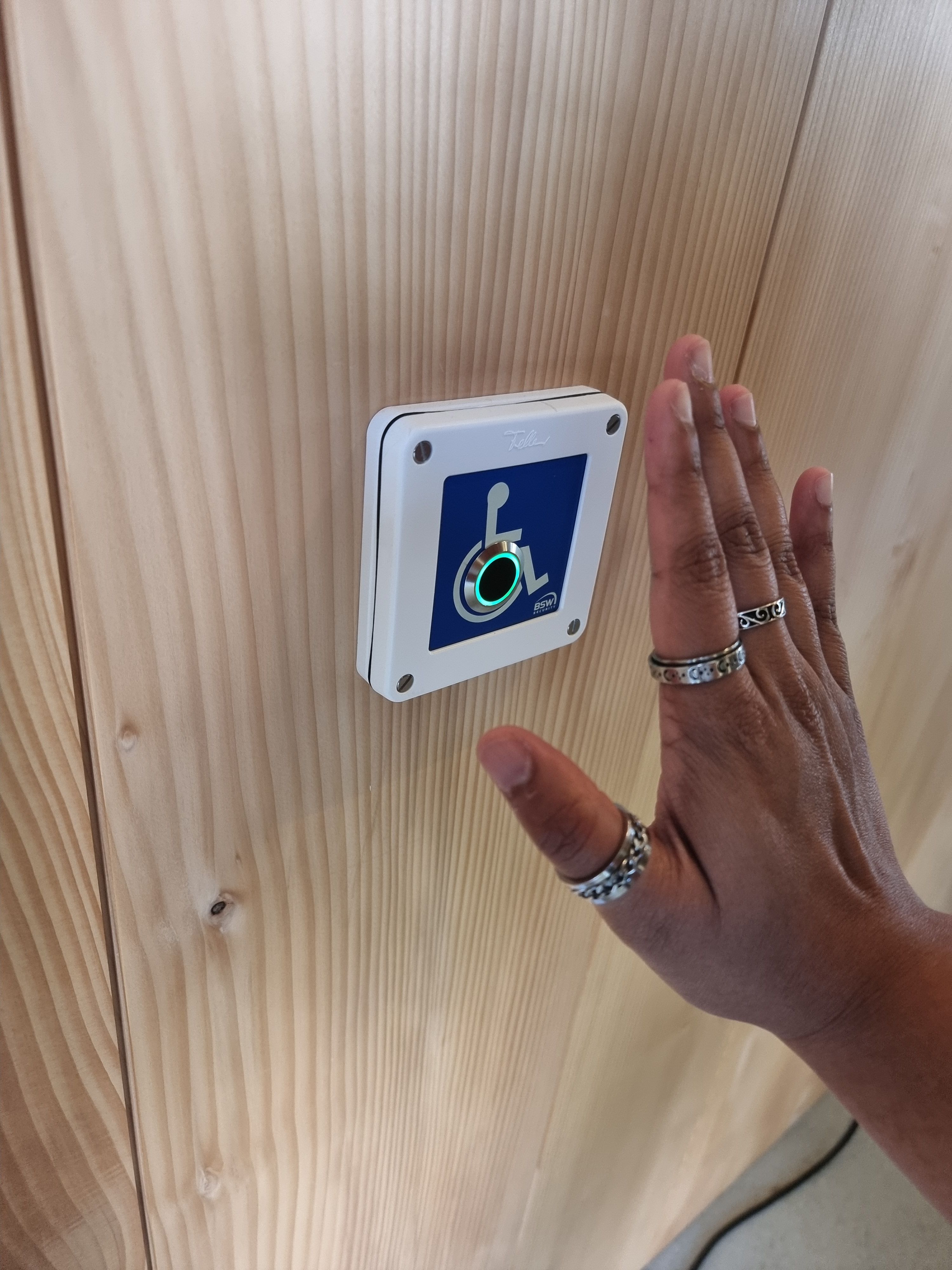 SOB Gebäude Erdgeschoss: Auf dem Bild sieht man eine Hand, die den Sensor für den barrierefreien Eingang betätigt. Leuchtet der Rand des Sensors grün, öffnet sich die Tür automatisch.