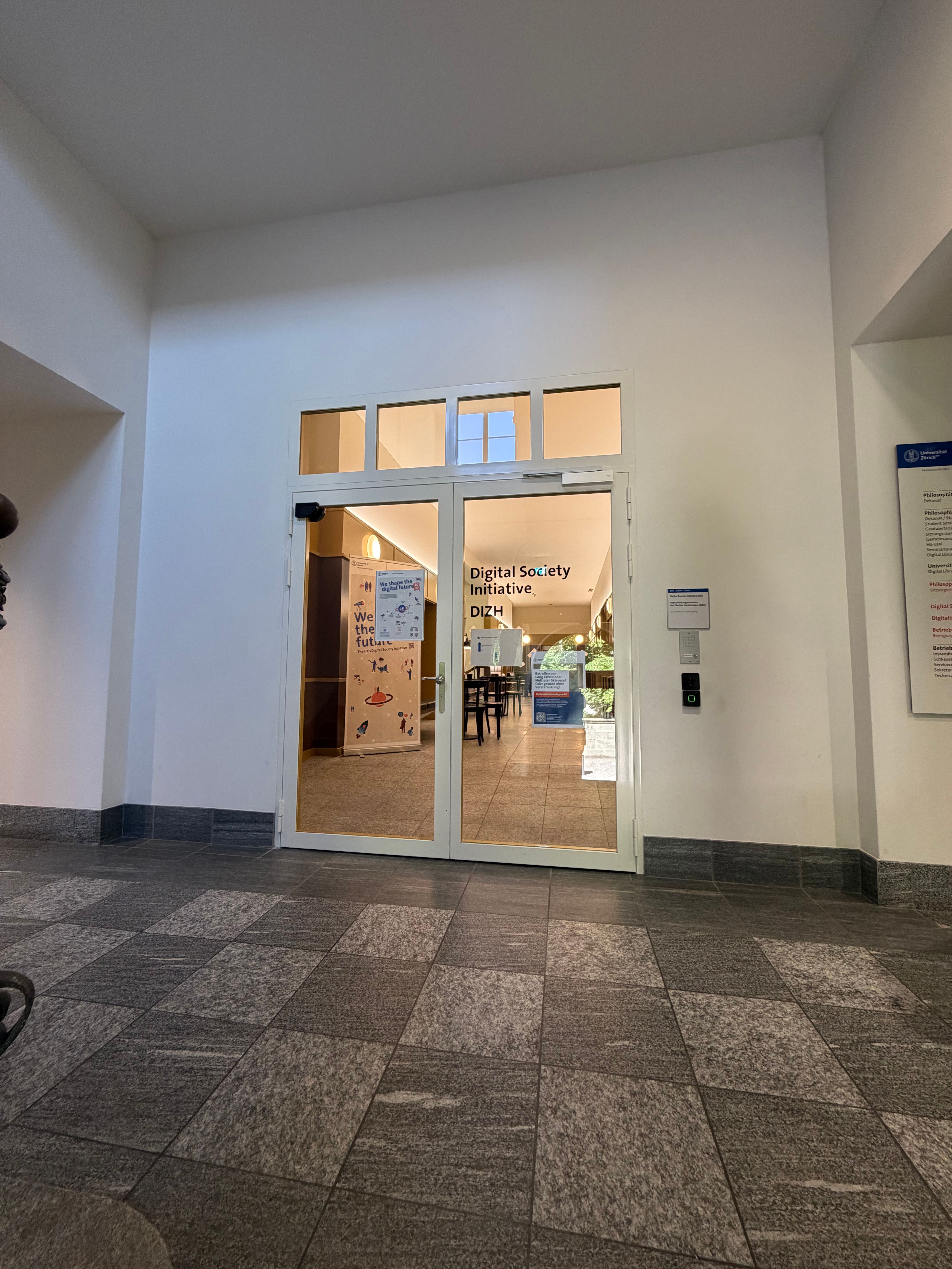 SOC_Stockwerk E (= EG): Sicht auf die Zugangstür zu den Räumlichkeiten der Digital Initiative Society (DIS) der Universität Zürich und der Digitalisierungsinitiative der Zürcher Hochschulen (DIZH). Die Zugangstür ist aus Glas und entsprechend transparent. Der Zugang ist ausschliesslich via Badge möglich. Zugang muss angefordert werden.