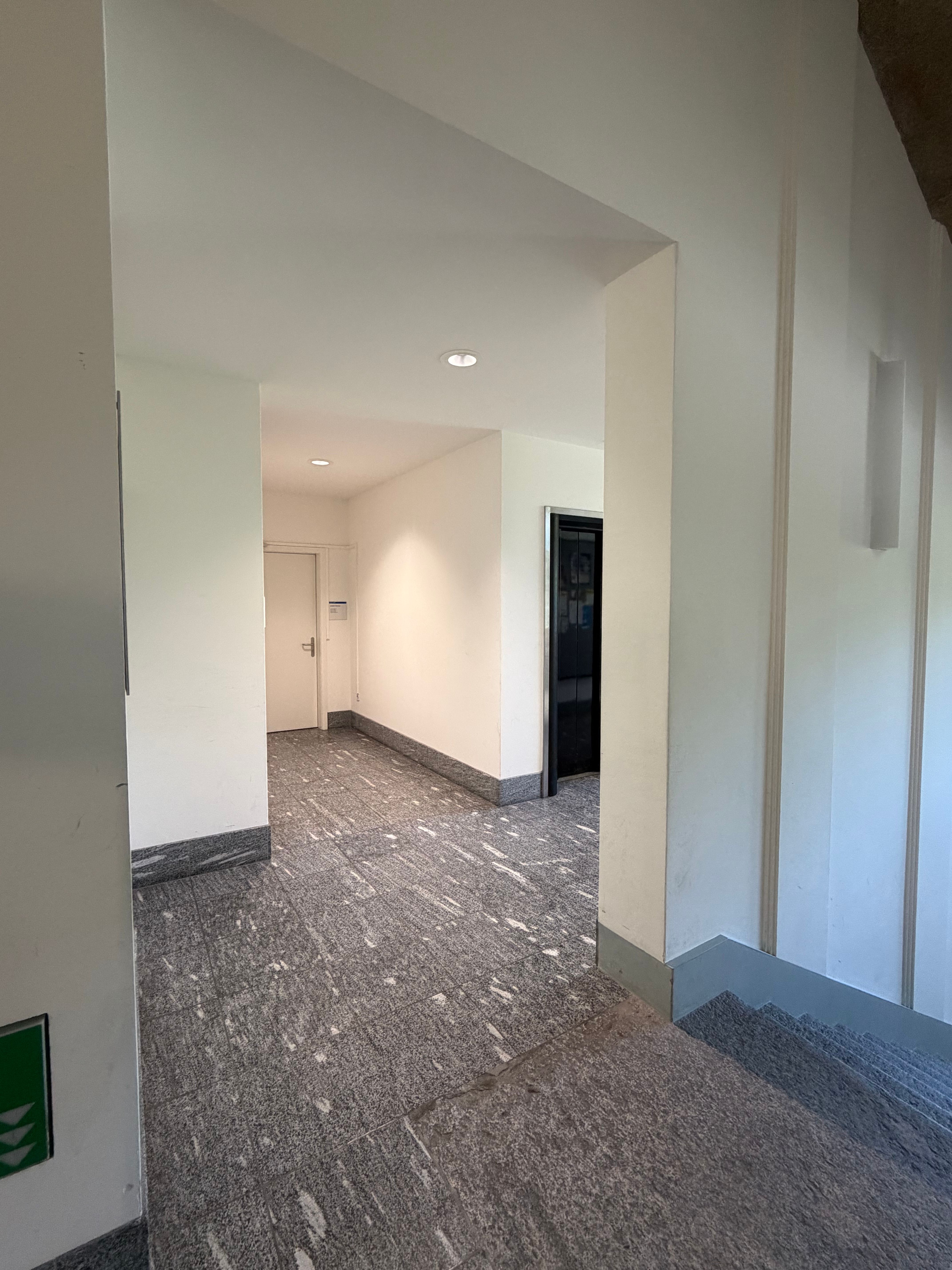 SOC_Stockwerk F (= 1. OG):  Man sieht den Gang, in dem der Lift im ersten OG vorhanden ist. Fotografiert vom Treppenhaus aus mit Sicht auf das Büro "Student Services" (Raum SOC-F-108b) der philosophischen Fakultät. Der Lift ist auf der rechten Seite abgebildet, davor die Treppe, die nach unten geht. Links führt der Weg zur Damentoilette.