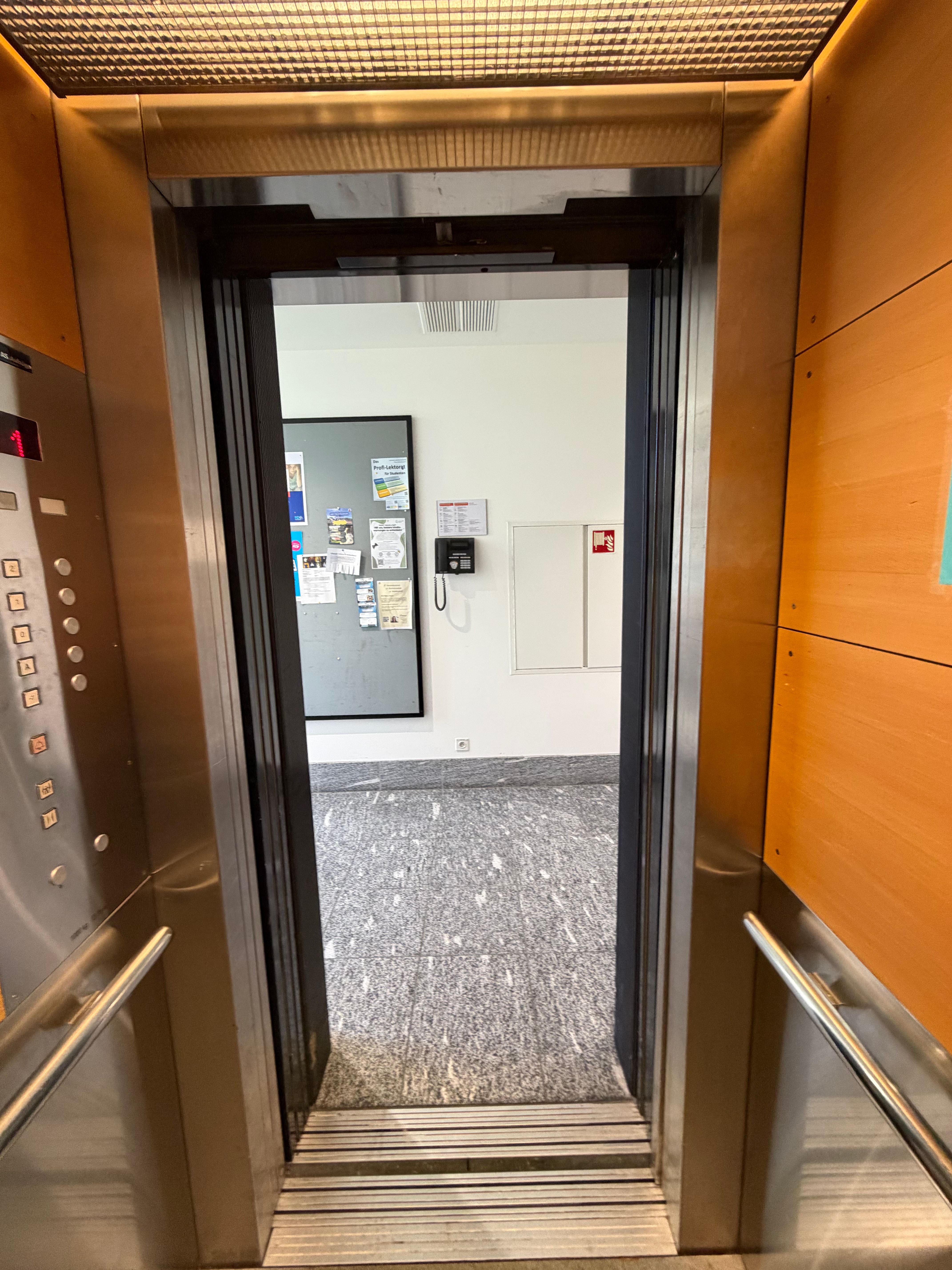 SOC_F (= 1. OG): Blick aus dem Lift auf den Gang im ersten Obergeschoss (Stockwerk F). Keine Stufen vorhanden.