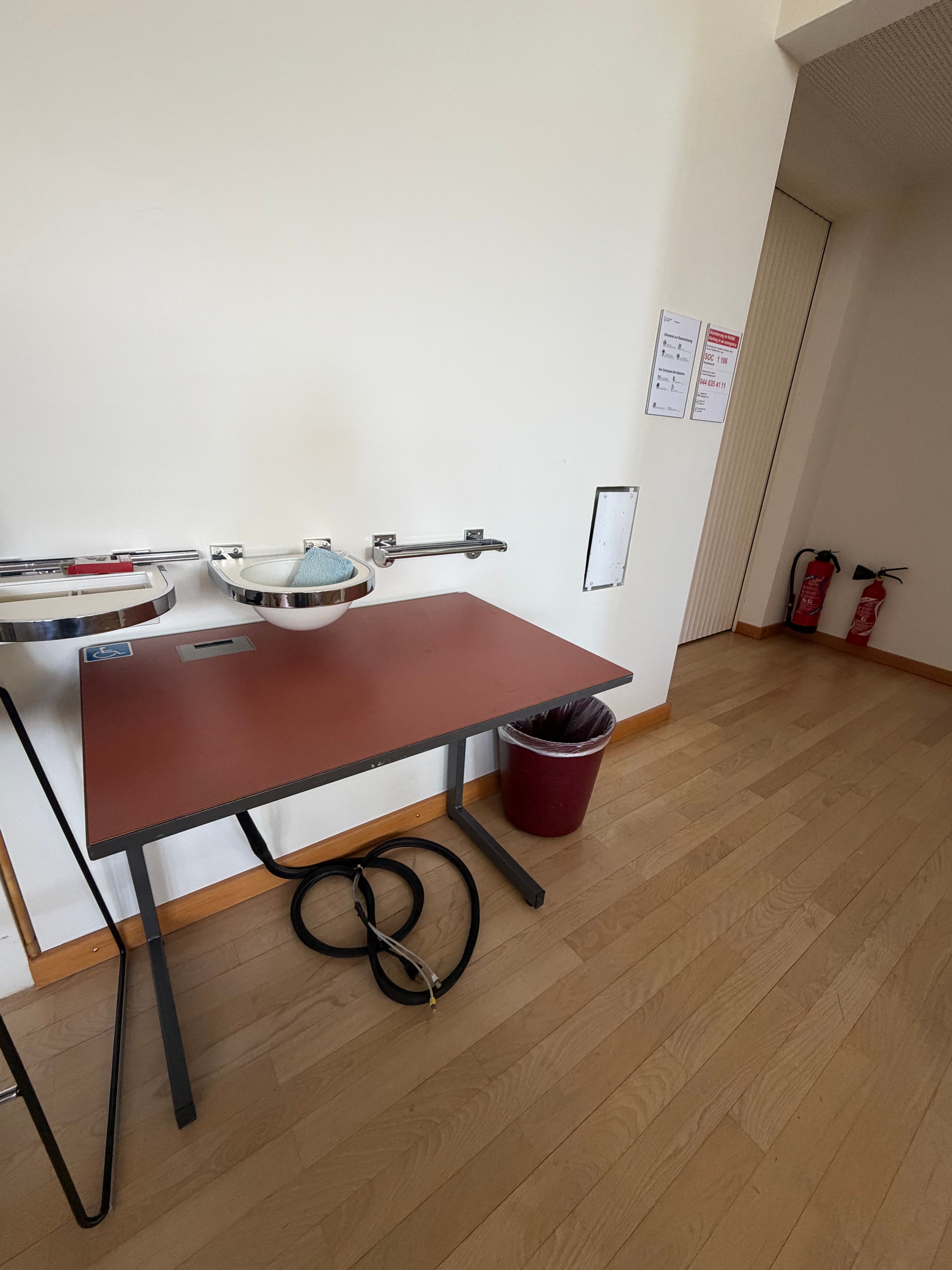 SOC F-106: Der Rollstuhltisch ist im Hörsaal vorne bei der Tafel abgestellt. Er ist mobil und kann bei Bedarf an einen geeigneten Platz verschoben werden.