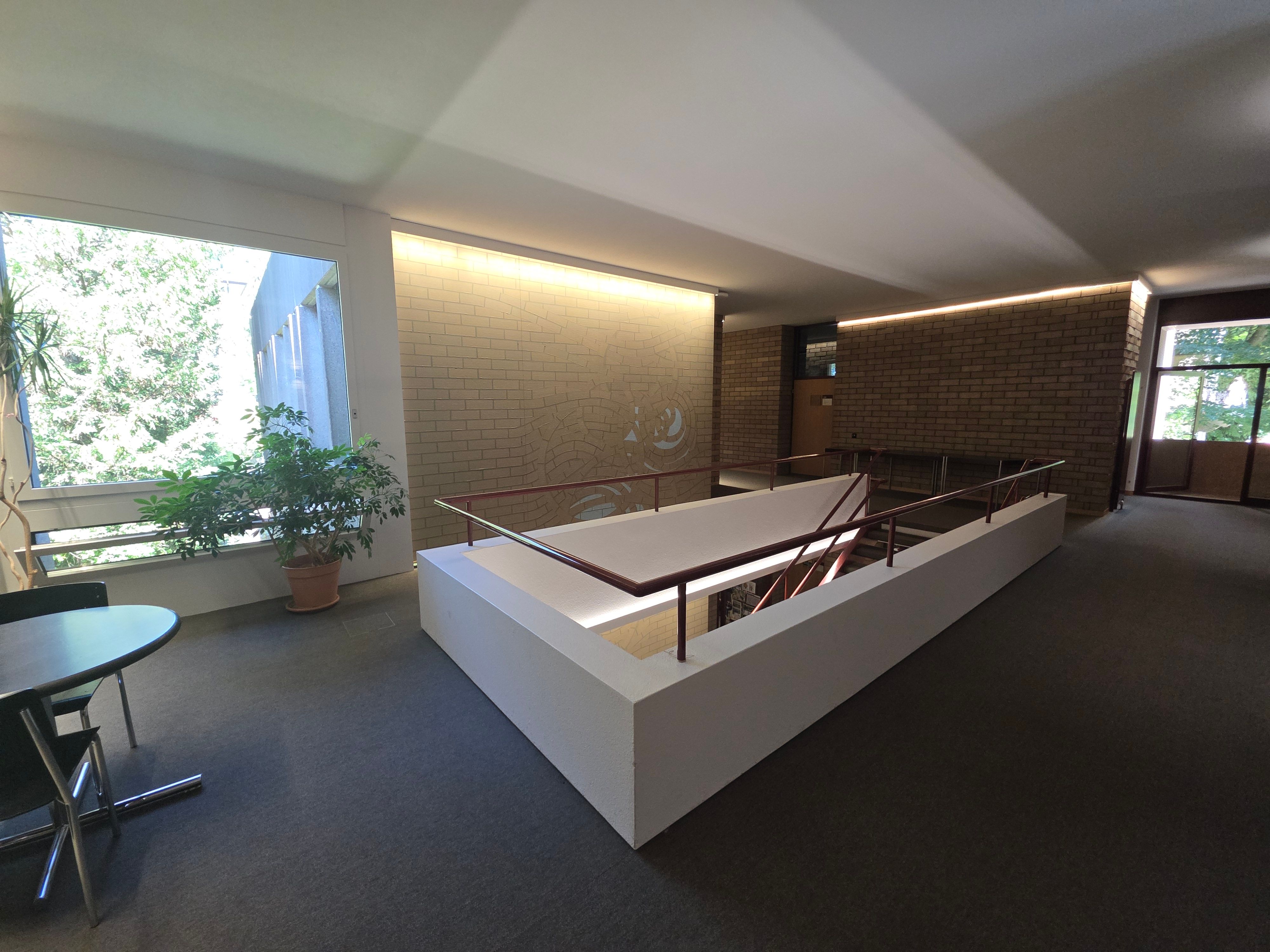PLG Stockwerk C: Ansicht des Stockwerks. In der Mitte vom Bild sieht man die Treppe, die nach unten zum Stockwerk B führt. Im Hintergrund sieht man die offene Tür von einem kleinen Balkon.