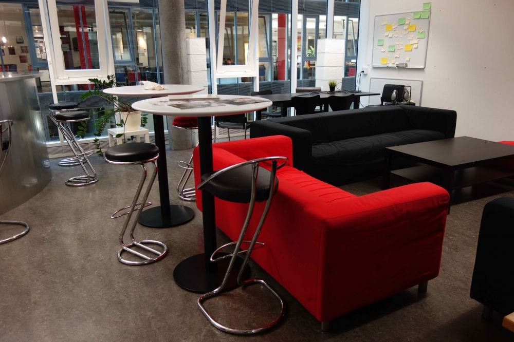 Aufenthaltsraum AND-2-11: Sofas und Stehtische mit Hockern. Im Hintergrund sind die Arbeitstische zu erkennen.