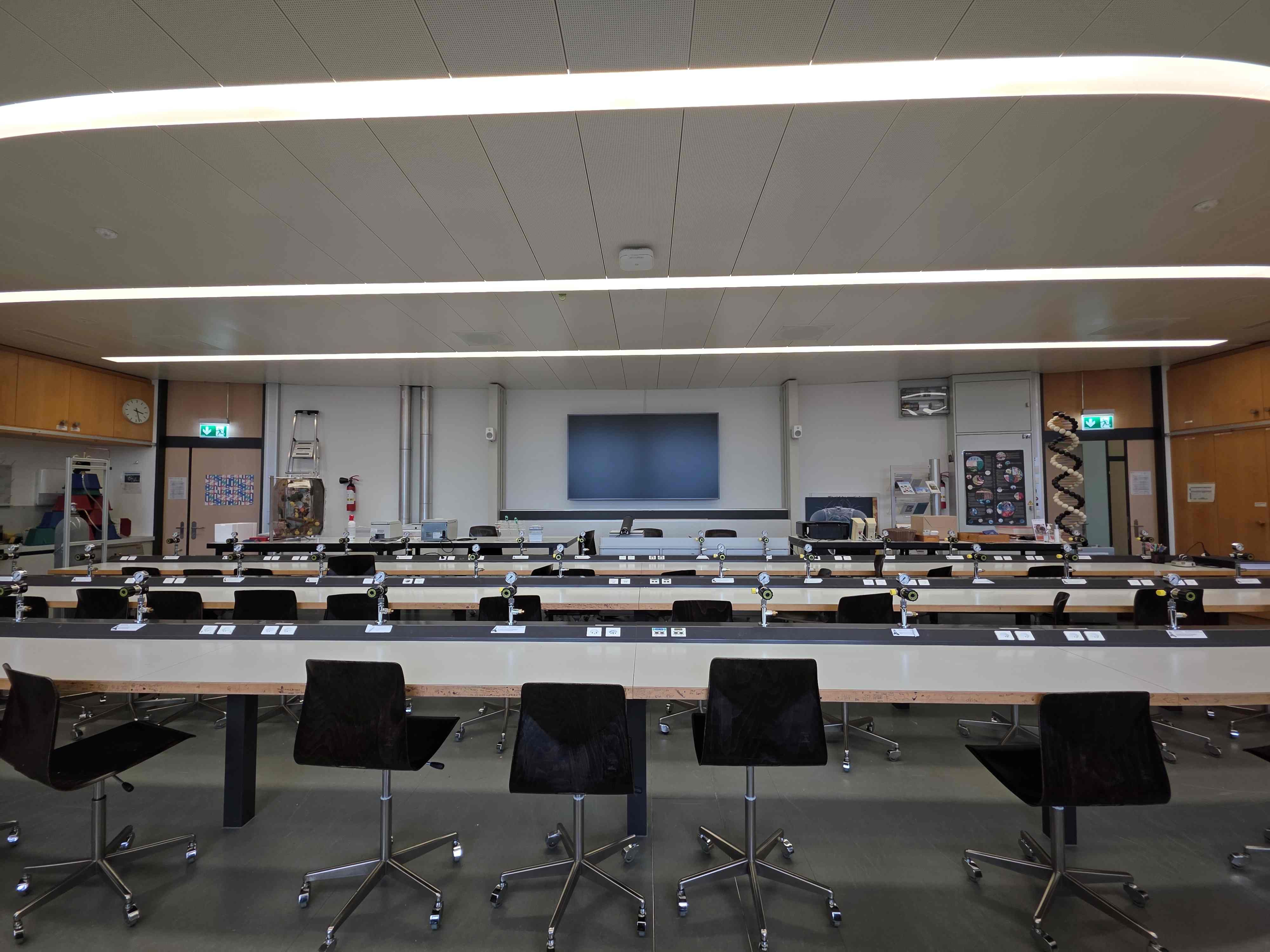 Labor Y17-L-05: Blick von der Mitte des Zimmers nach vorne auf die Tafel. Der Raum hat drei Sitzreihen. Die zwei Ausgänge sind auf der linken und rechten Seite vom Dozierendenpult.