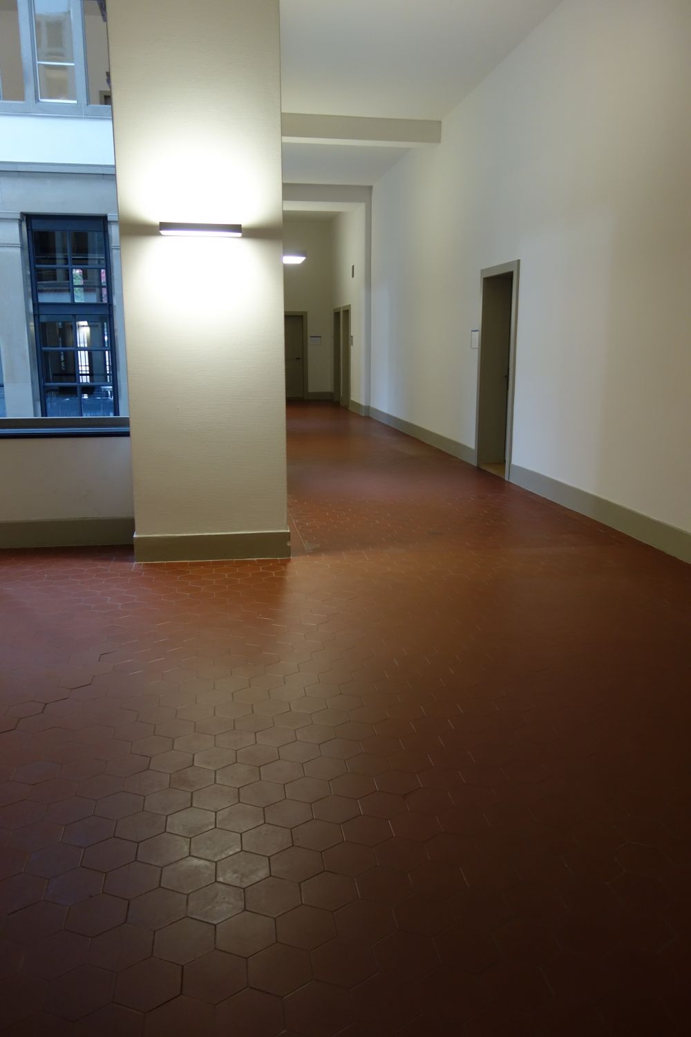 Rollstuhl-WC RAA-E-24: Blick Richtung Rollstuhl-WC vom Gang her. Das WC befindet sich am Ende des Ganges auf der rechten Seite. Links im Bild ist der Lichthof zu erkennen.