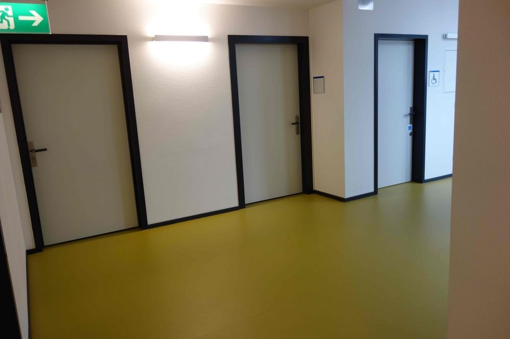 Rollstuhl-WC RAA-H-24: Blick vom hinteren Gang her Richtung Rollstuhl-WC. Das WC befindet sich bei der Tür ganz rechts.