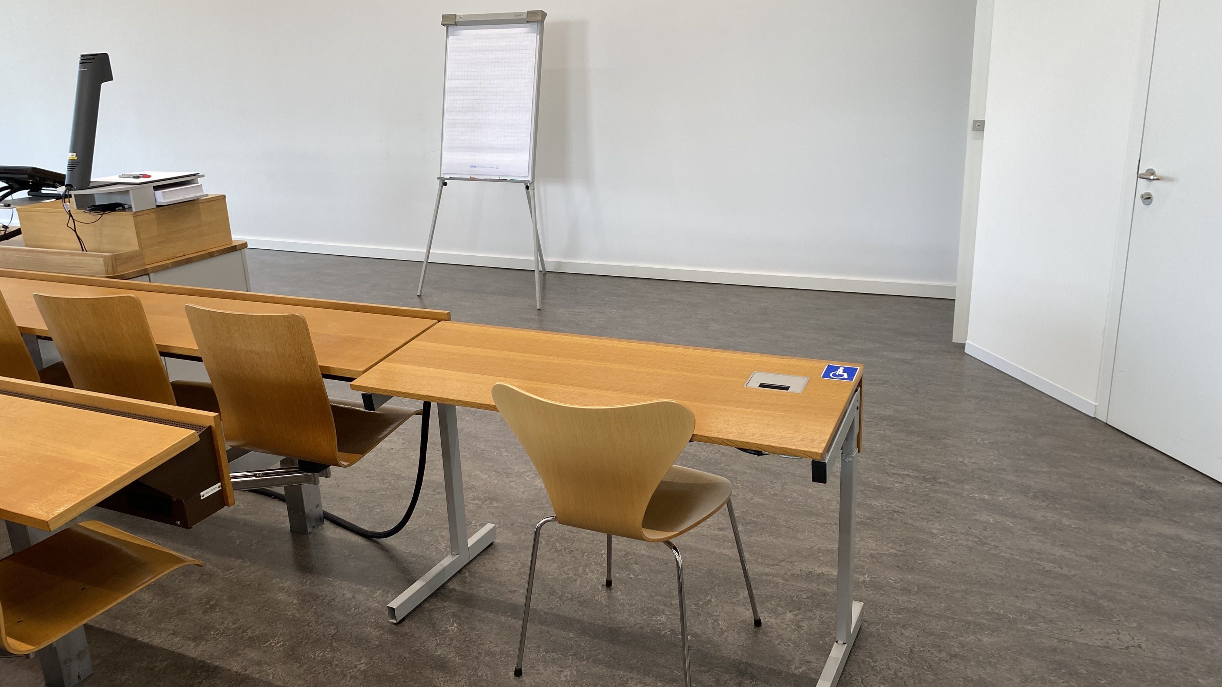 Hörsaal RAI-H-041: Ansicht auf den ersten von zwei Tischen mit Rollstuhl-Signet in der vordersten Reihe ohne fixe Bestuhlung. Dieser Tisch befindet sich direkt neben der Eingangstüre auf der rechten Seite des Raumes.