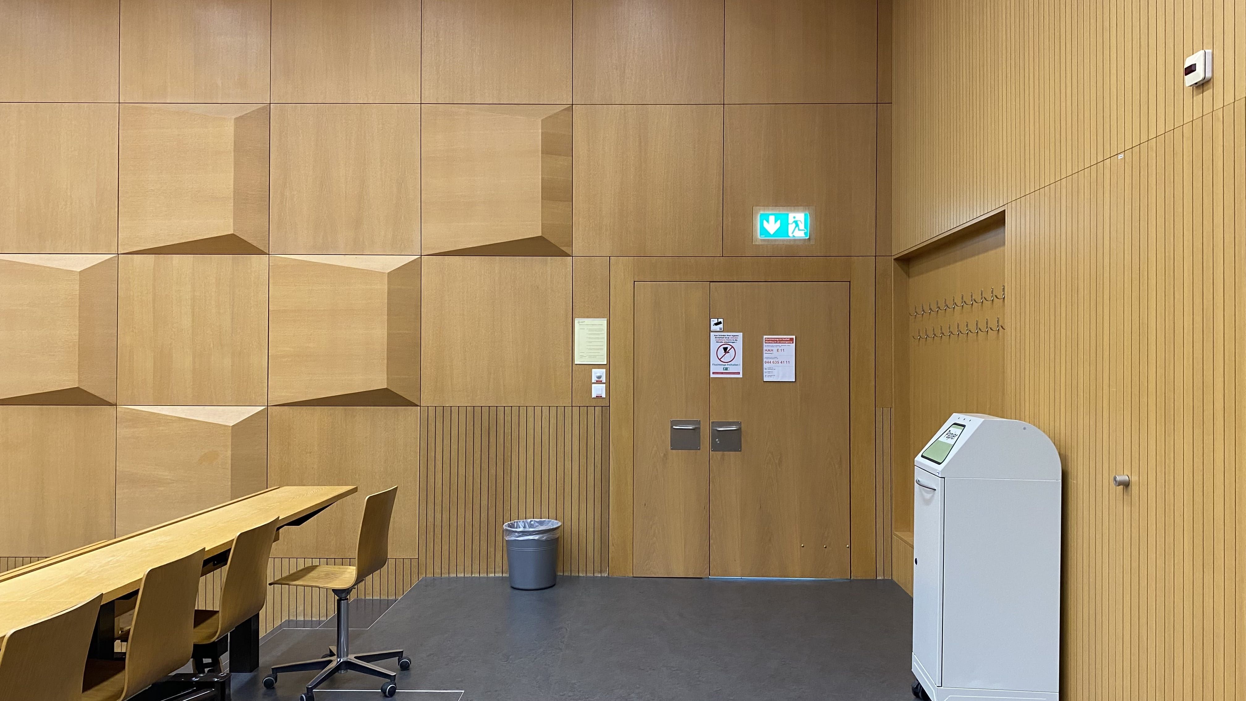 Hörsaal HAH-E-11: Ansicht auf die linke Eingangstüre in der obersten Reihe. Auf der gegenüberliegenden Seite befindet sich ebenfalls eine Eingangstüre.