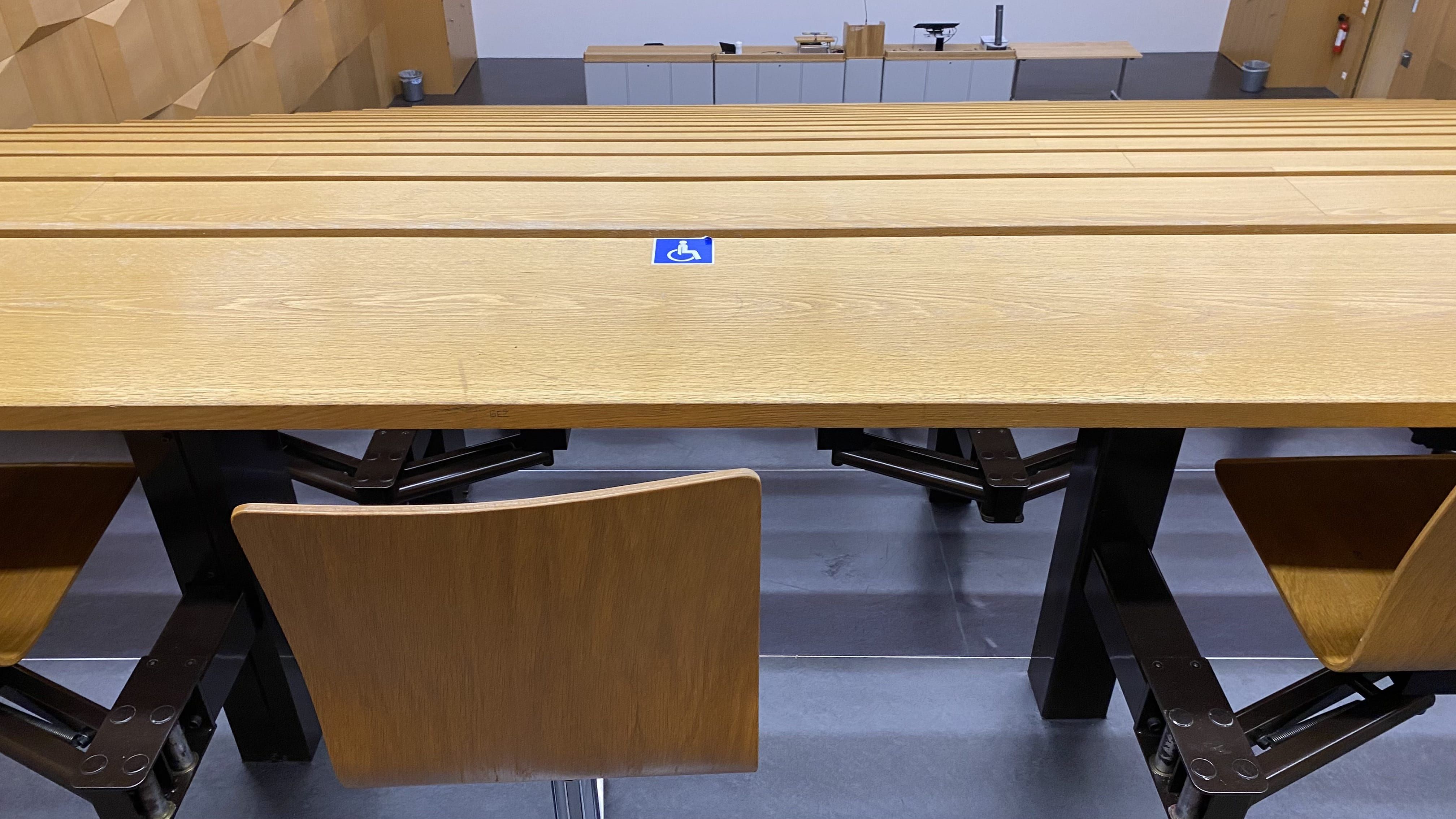 Hörsaal HAH-E-11: Der zweite von vier Plätzen ohne fixe Bestuhlung, mit Rollstuhl-Signet, in der obersten Reihe. Dieser Platz befindet sich links von der Mitte.