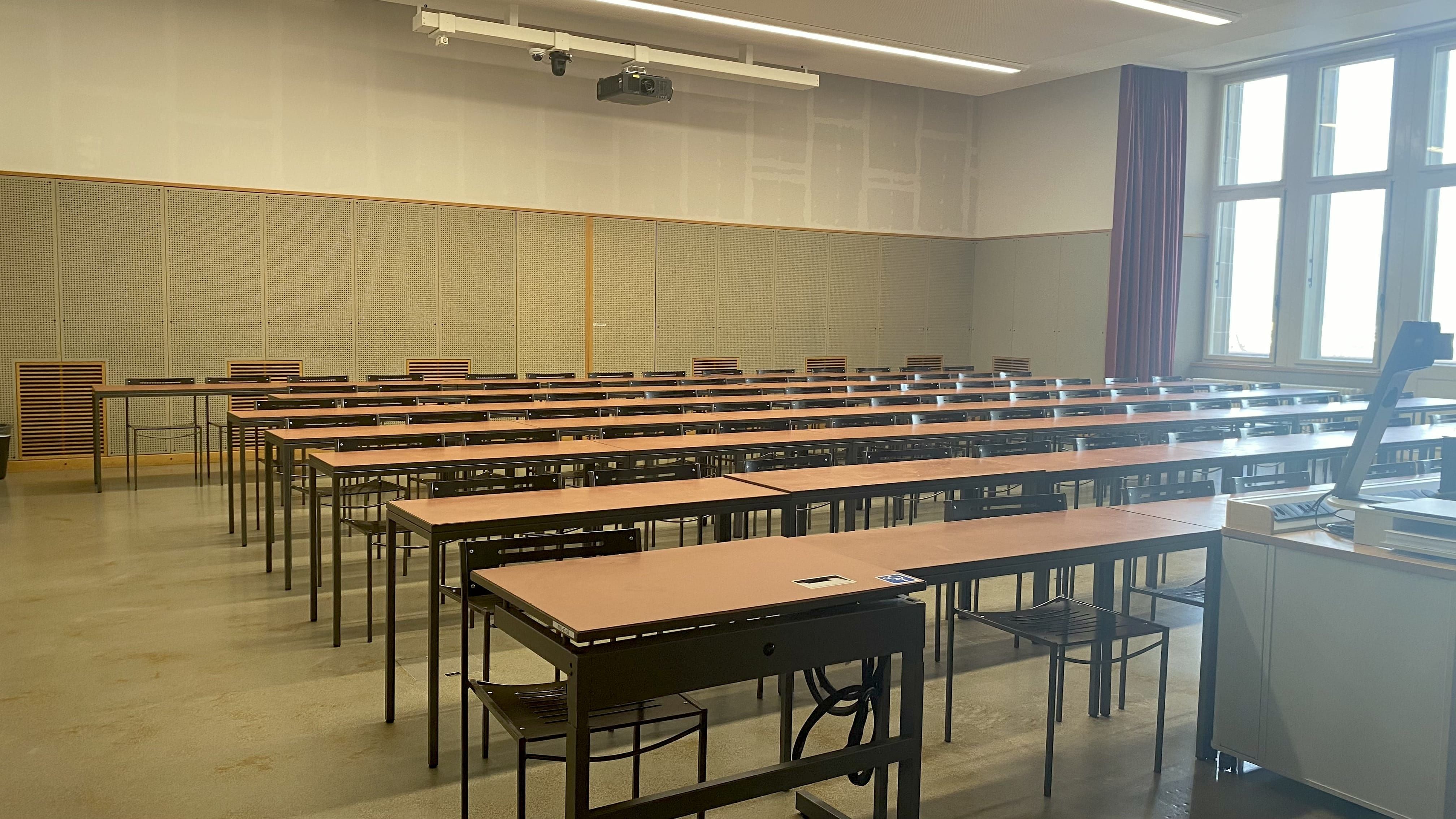 Hörsaal KOL-E-18: Ansicht auf den Raum von der Eingangstür aus. In der vordersten Reihe auf der linken Seite im Bild befindet sich ein elektrisch verstellbarer Tisch mit Rollstuhl-Signet.