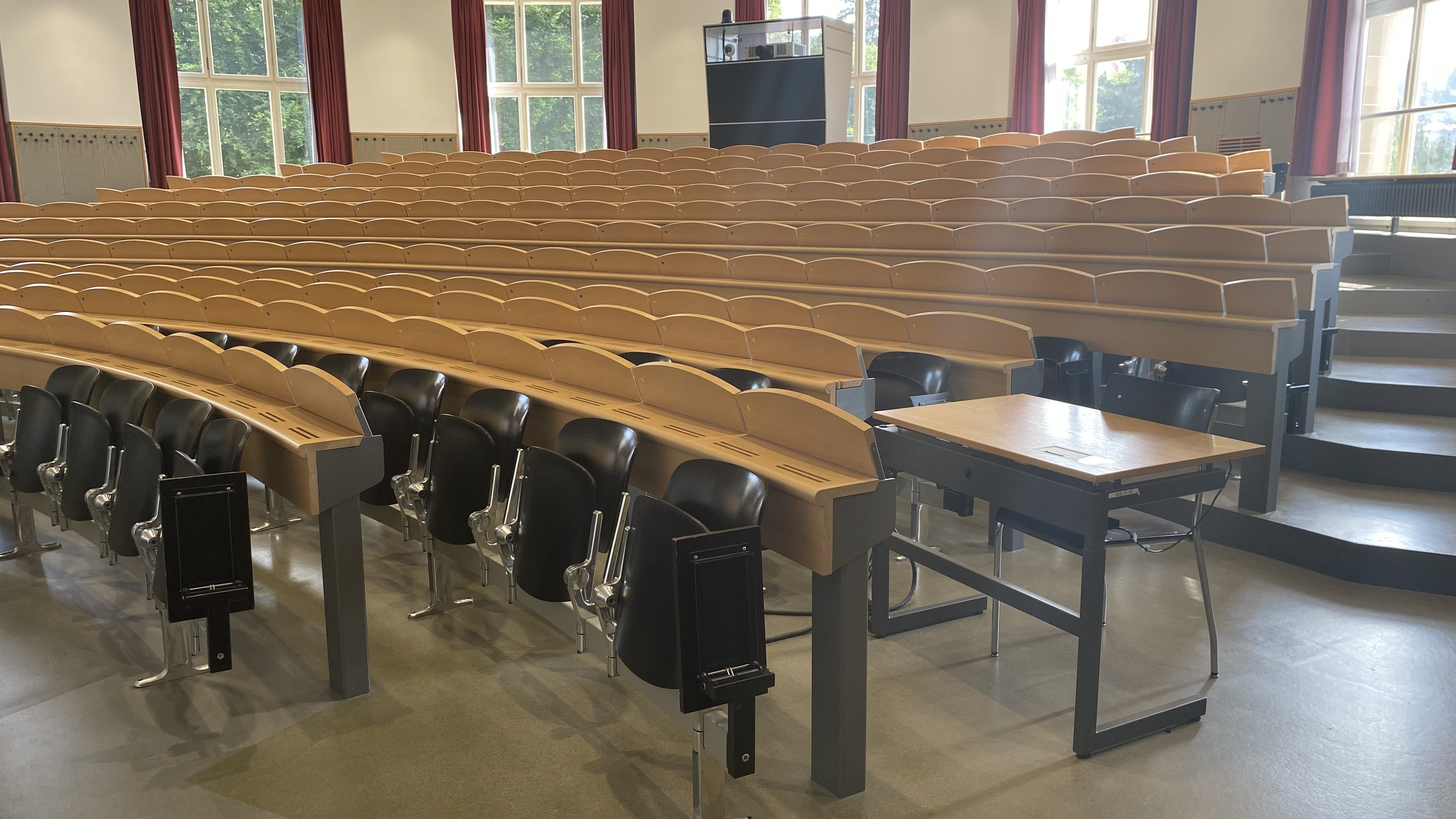 Hörsaal KOL-F-101: Ansicht auf den Raum von der rechten Eingangstür aus. Auf dieser Seite befindet sich ein elektrisch höhenverstellbarer Tisch mit Rollstuhl-Signet in der dritten Reihe.