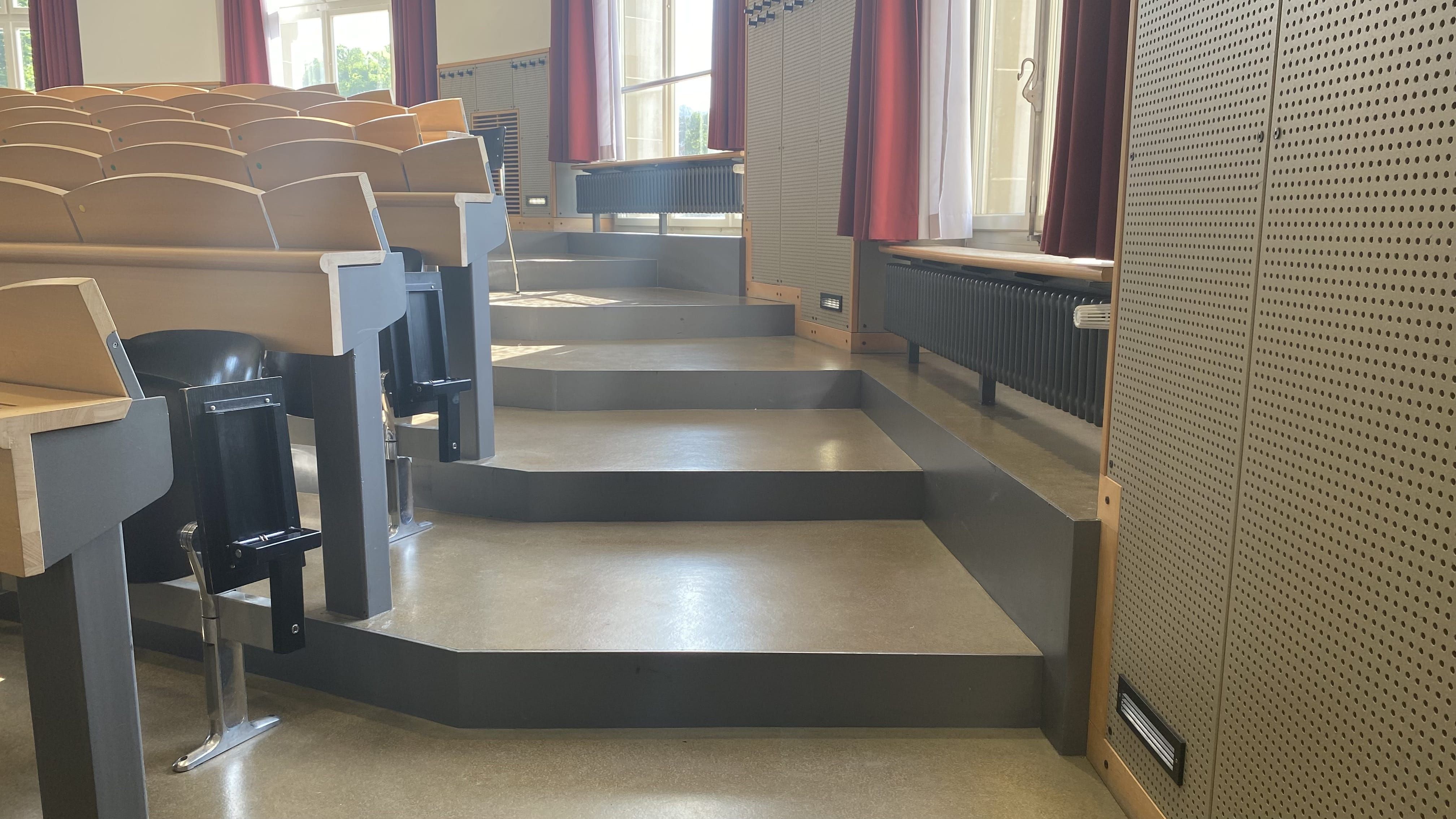 Hörsaal KOL-F-101: Ansicht auf die Stufen, die links und rechts im Raum zu den hinteren Sitzreihen führen. Die Stufen sind nicht mit Orientierungshilfen markiert.
