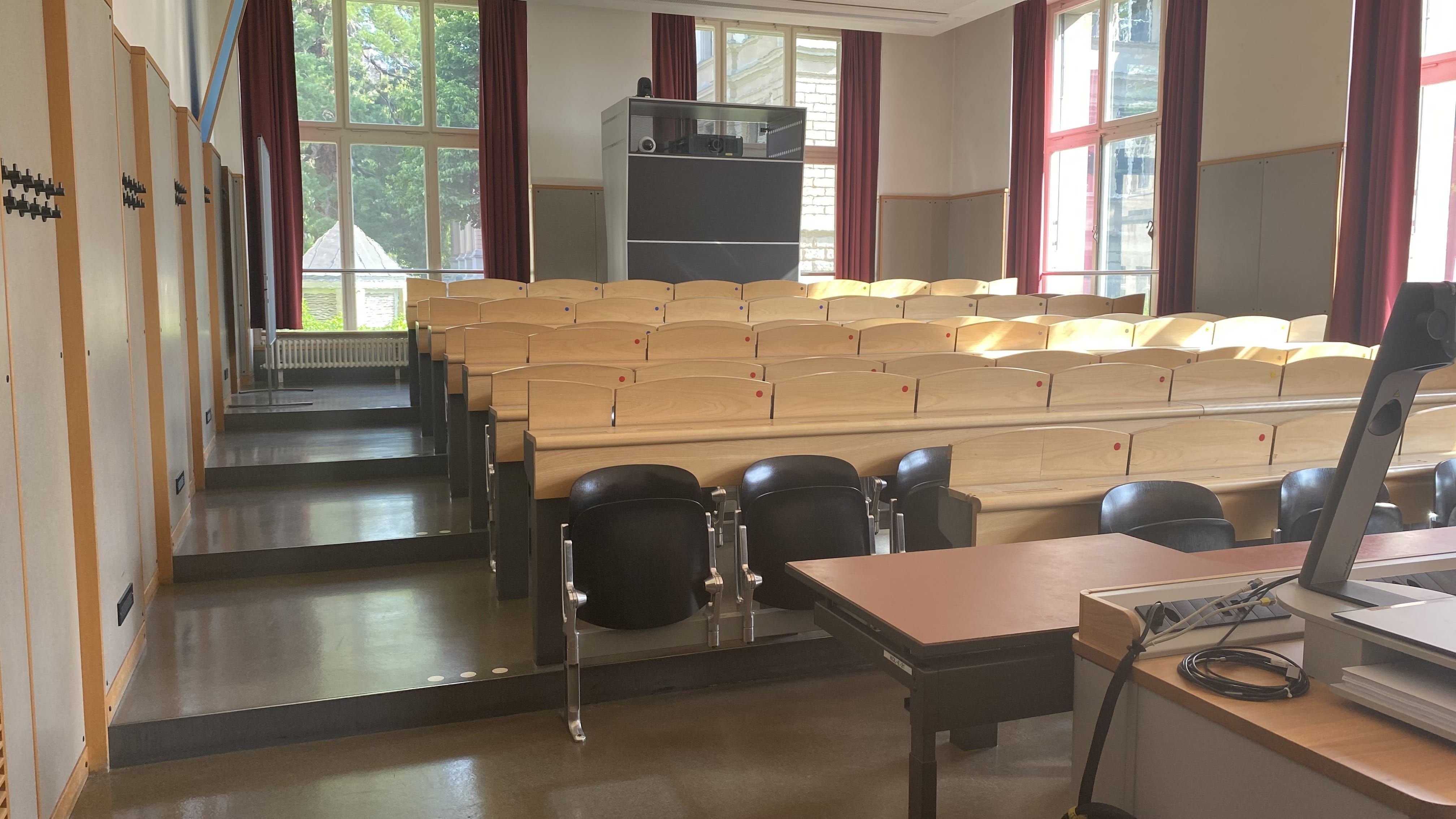 Hörsaal KOL-E-21:  Ansicht auf den Raum von der Eingangstür aus. Ein elektrisch höhenverstellbarer Tisch mit Rollstuhl-Signet befindet sich in der vordersten Reihe.