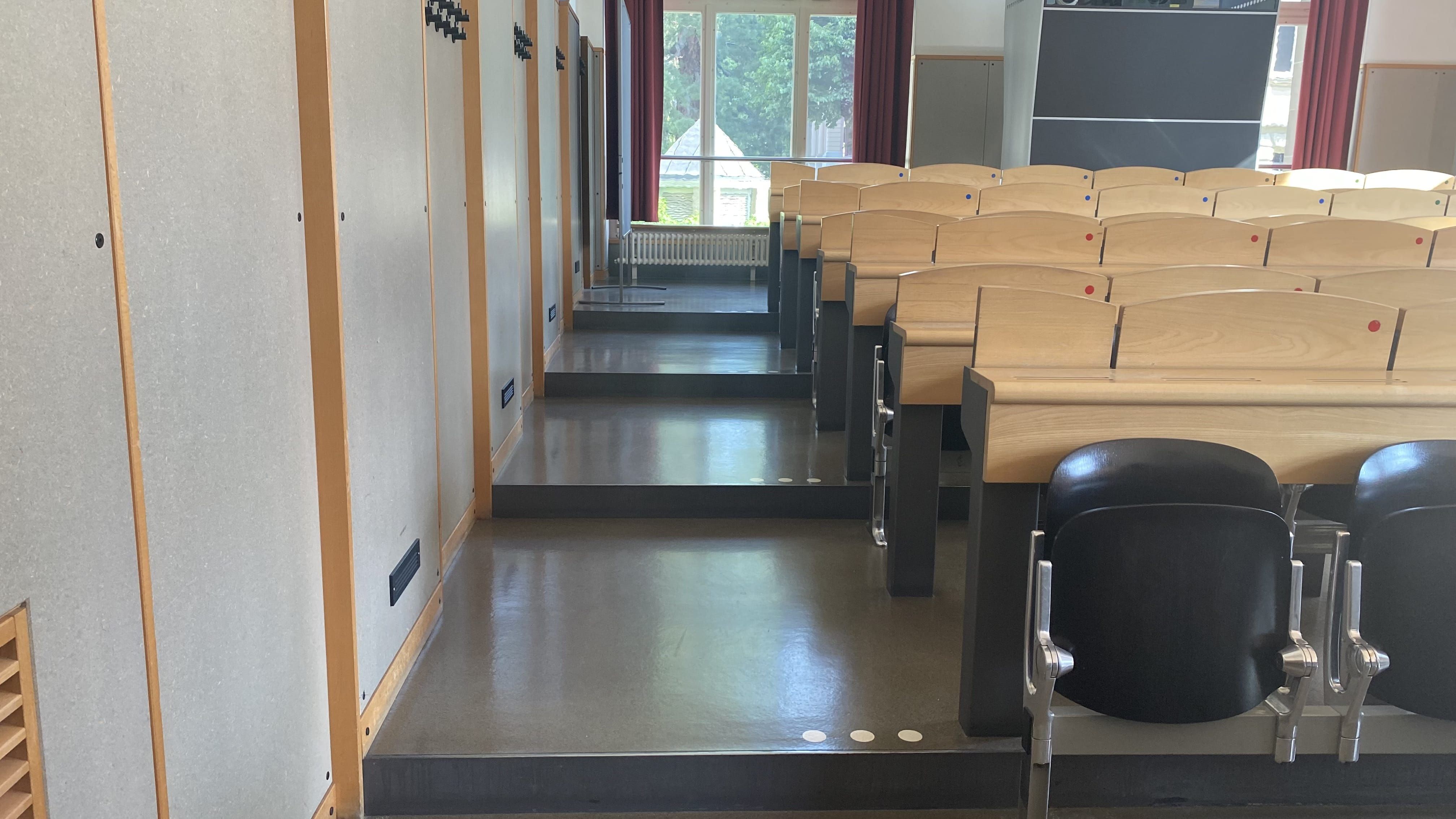 Hörsaal KOL-E-21: Ansicht auf den linken, breiten Durchgang. Die Stufen sind mit Orientierungshilfen markiert.