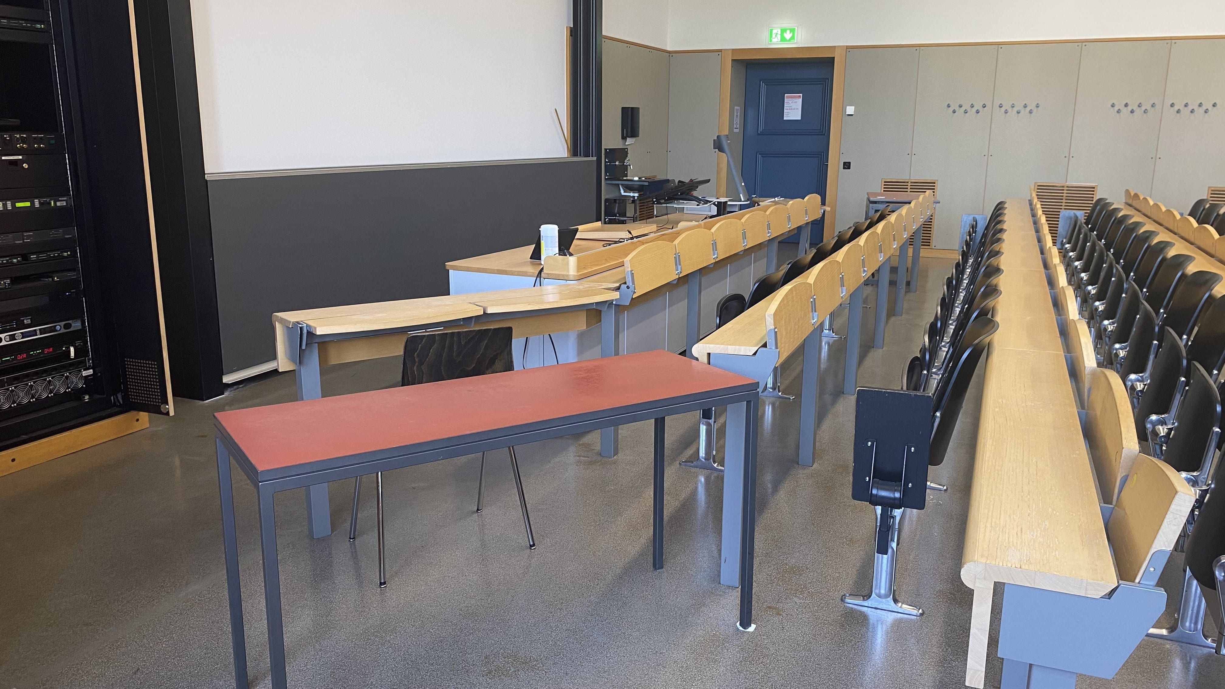 Hörsaal KOL-F-117: Ansicht auf die linke Seite des Raumes. Es gibt einen Tisch ohne fixe Bestuhlung.