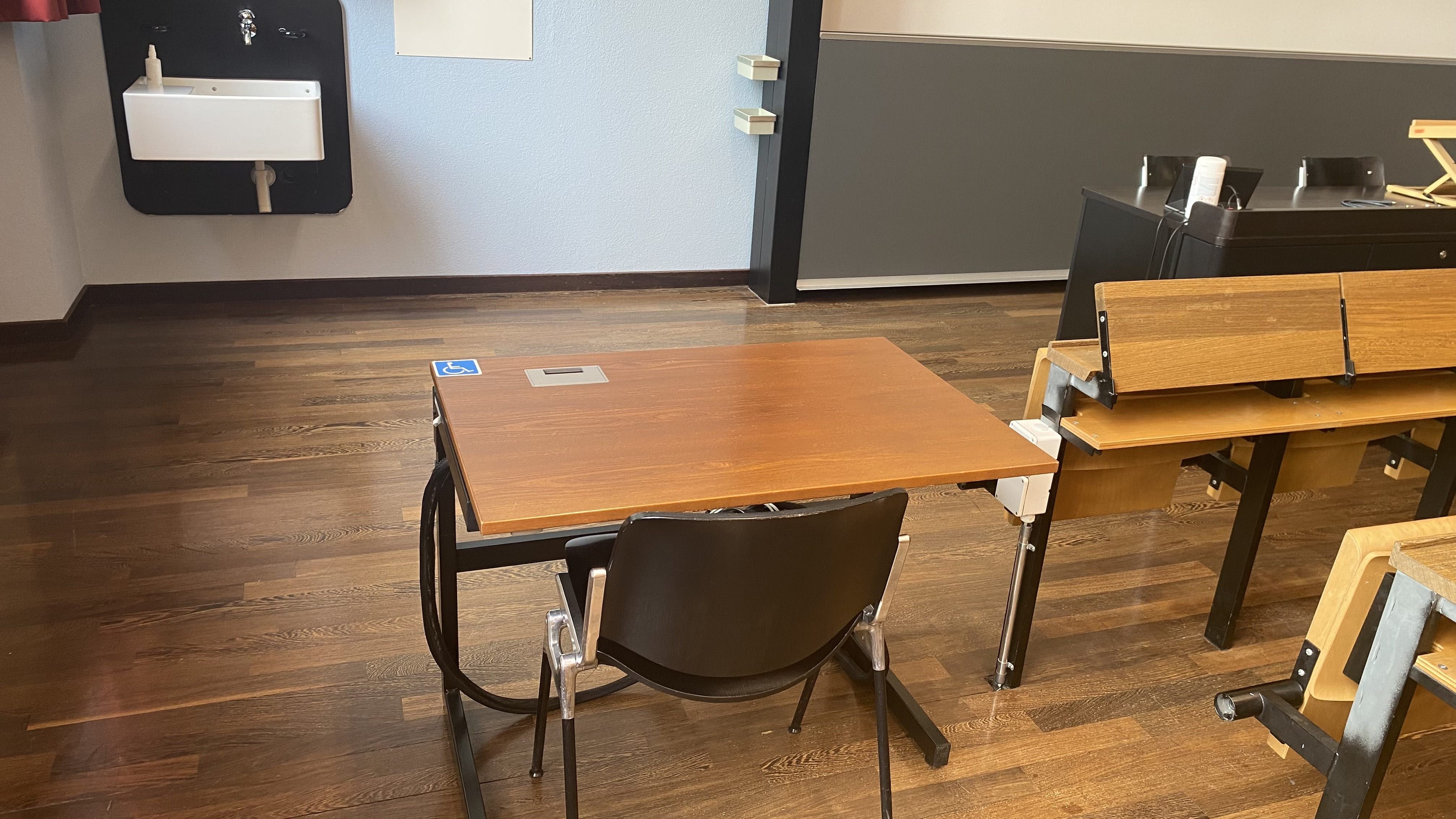 Hörsaal KOL-F-118: Ansicht auf den ersten von zwei elektrisch höhenverstellbaren Tischen mit Rollstuhl-Signet. Dieser Tisch befindet sich links im Raum in der vordersten Reihe.