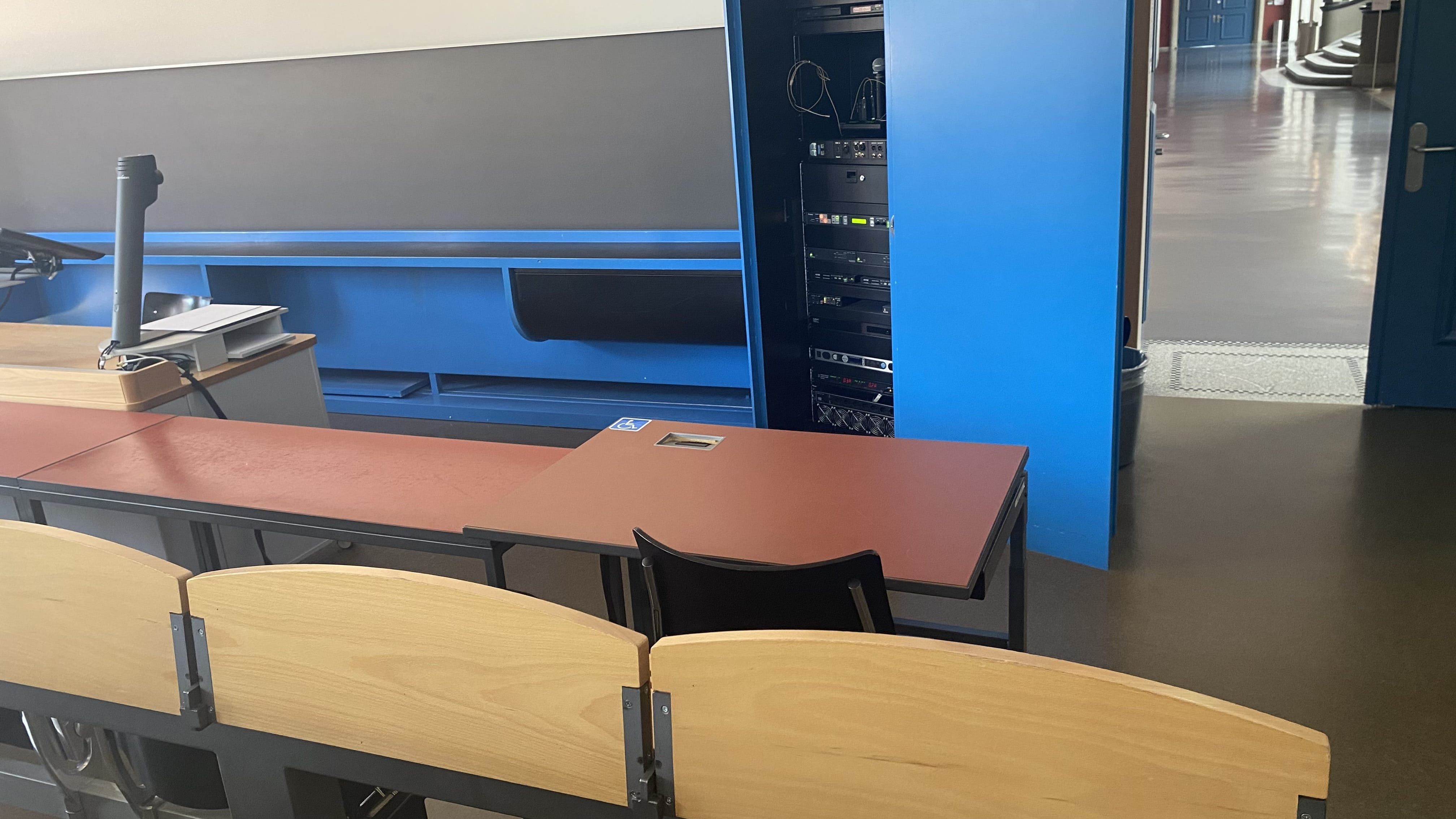 Hörsaal KOL-F-121: Ansicht auf den elektrisch höhenverstellbarer Tisch mit Rollstuhl-Signet. Der Tisch befindet sich in der vordersten Reihe rechts, nahe der Eingangstür.