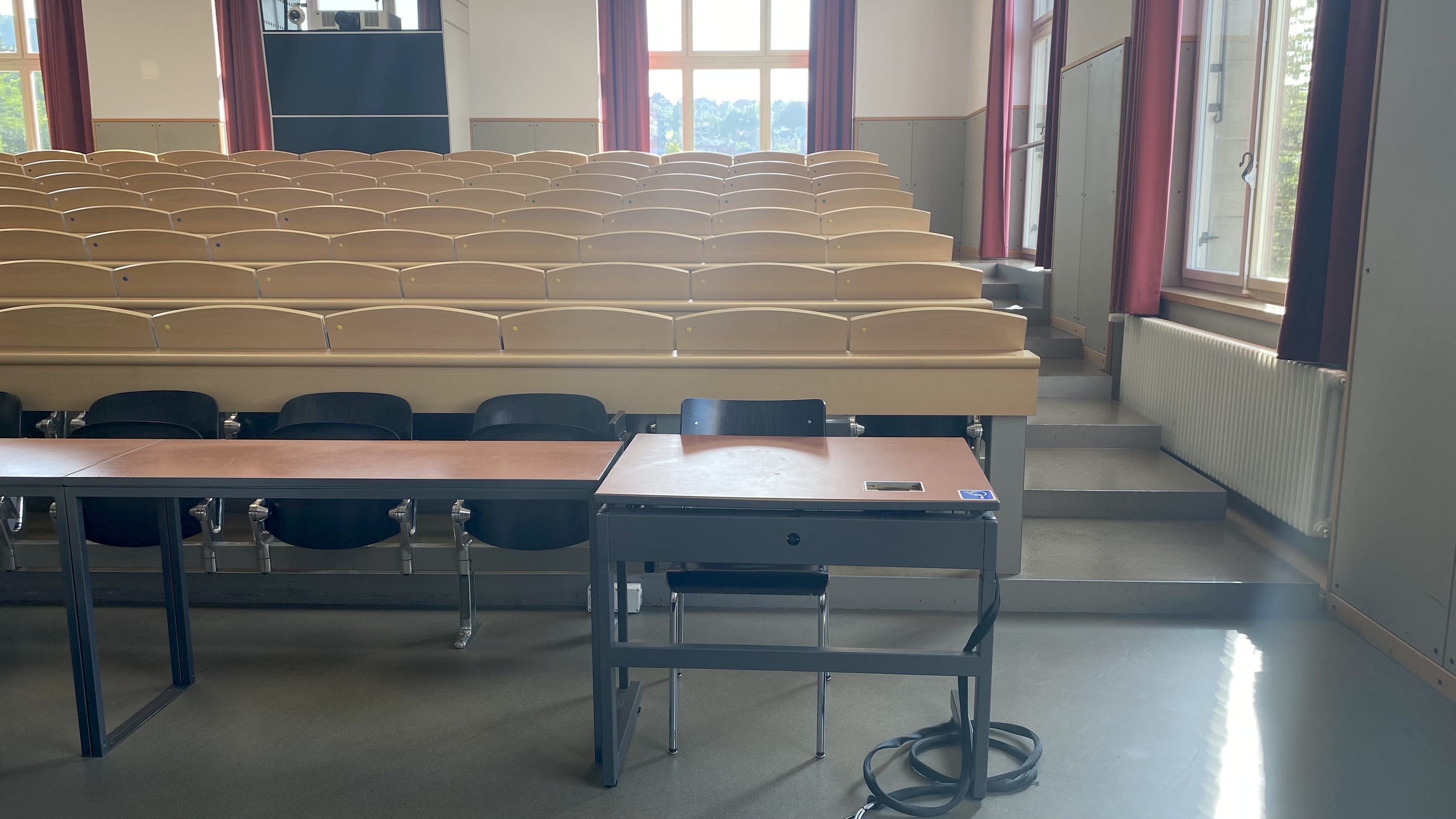 Hörsaal KOL-F-104: Ansicht auf den elektrisch höhenverstellbaren Tisch mit Rollstuhl-Signet. Der Tisch befindet sich auf der rechten Seite des Raumes in der vordersten Reihe.