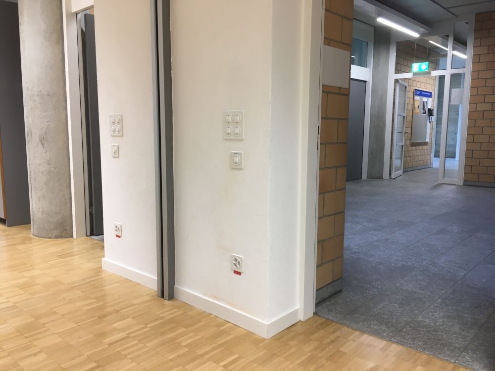 Seminarraum PLM-F-104: Steckdosen an der Wand zwischen den zwei Eingangstüren.