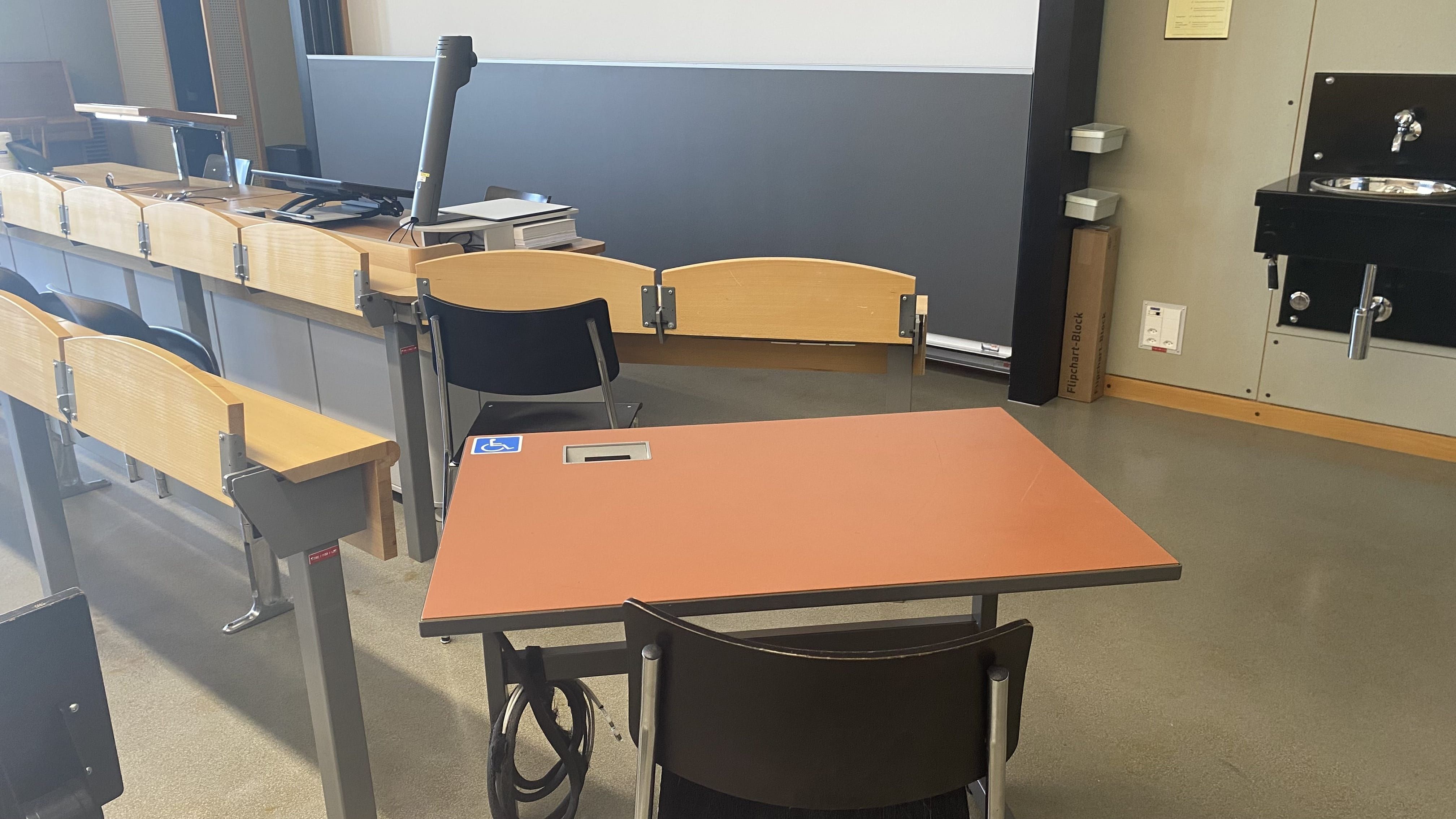 Hörsaal KOL-G-217: Ansicht auf den elektrisch höhenverstellbaren Tisch in der zweitvordersten Reihe, rechts, nahe an der rechten Eingangstür.