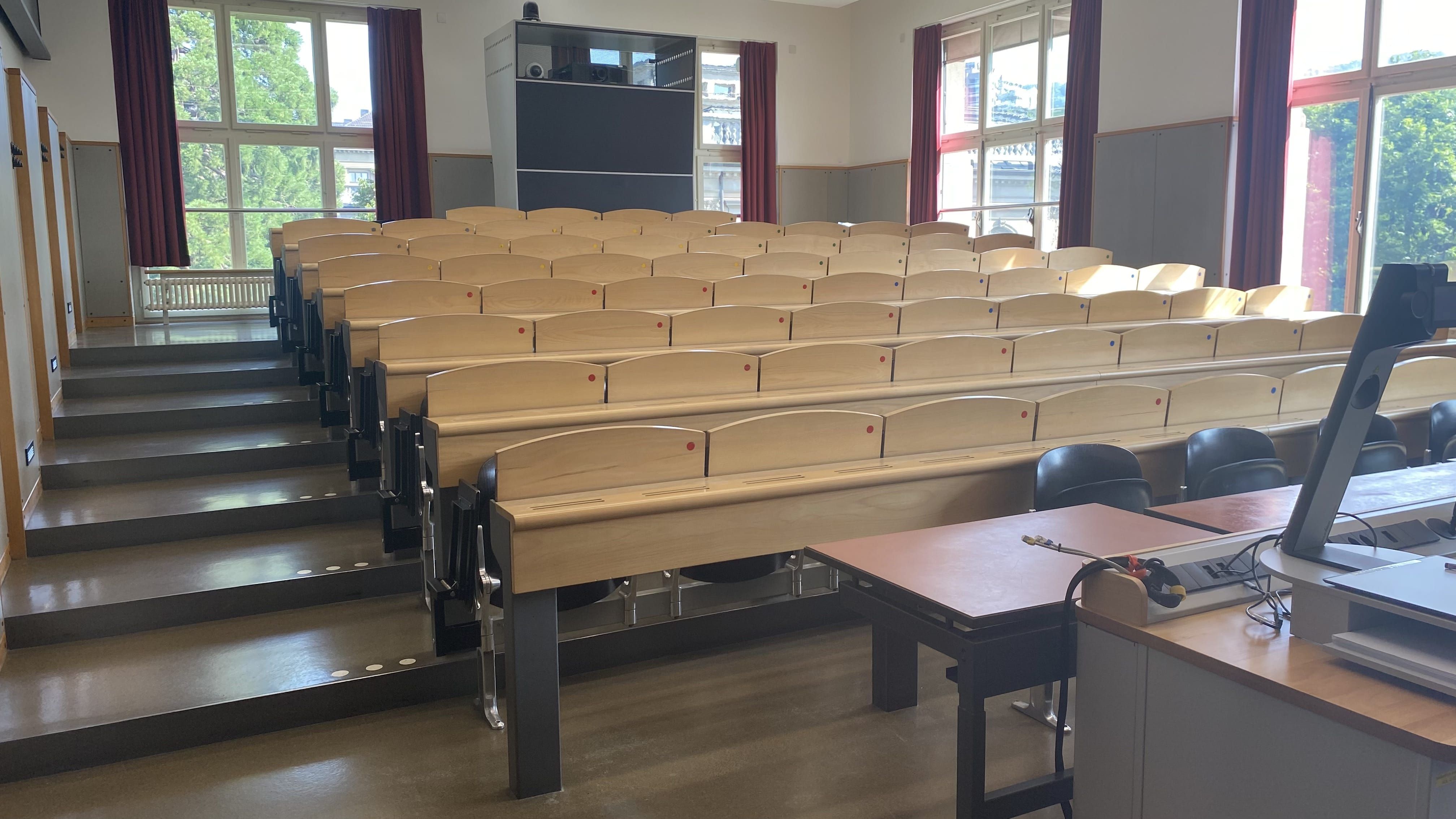 Hörsaal KOL-G-221: Ansicht auf den Raum von der Eingangstür aus. Die breiten Stufen links sind mit Orientierungshilfen markiert.