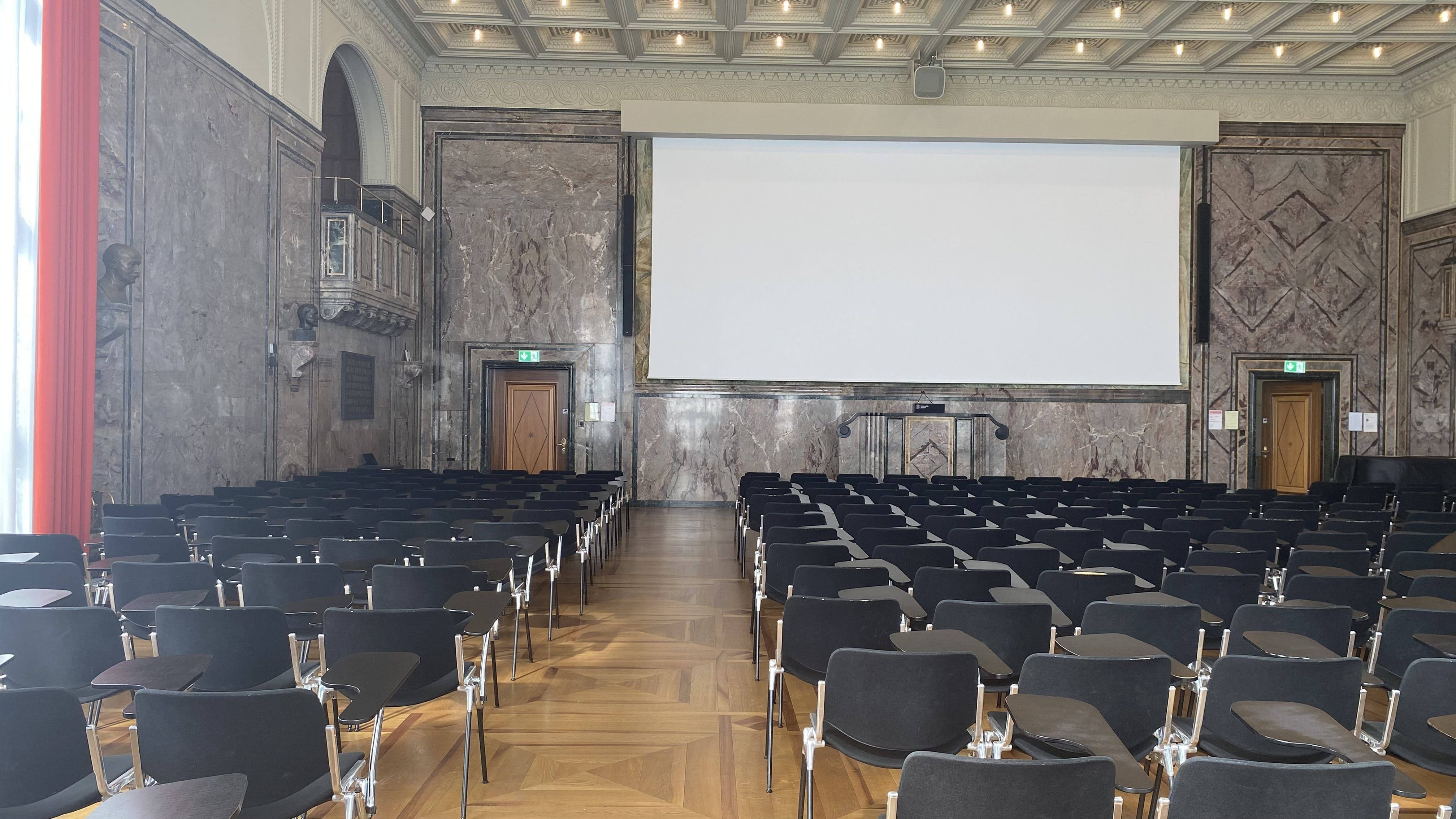 KOL-G-201, Aula: Ansicht zum Rednerpult hin. Die Eingangstüren befinden sich links, beziehungsweise rechts im Bild.