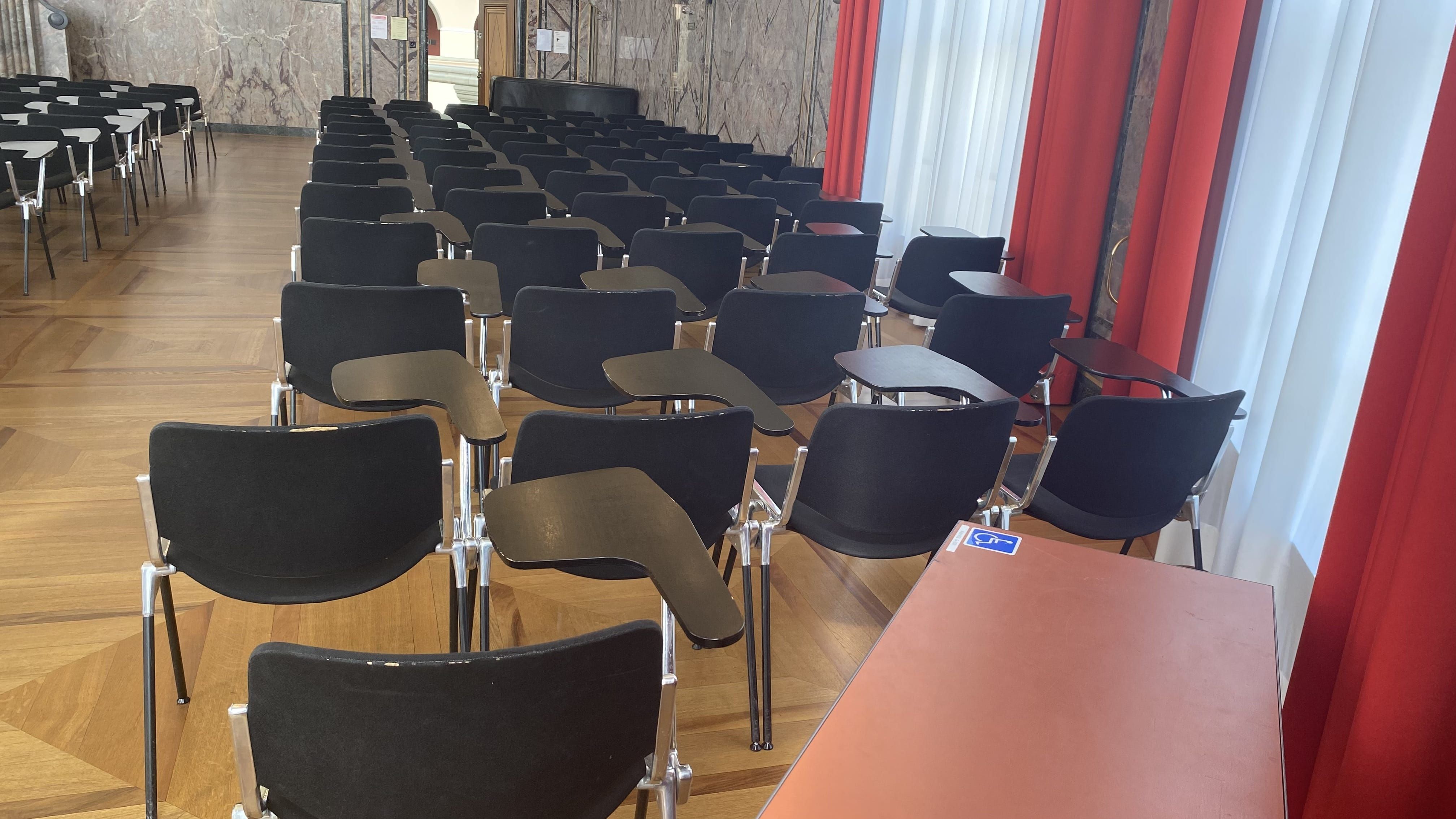 KOL-G-201, Aula: Ansicht auf einen Tisch mit Rollstuhl-Signet, der sich auf der linken Seite der Aula befindet und benutzt werden kann.