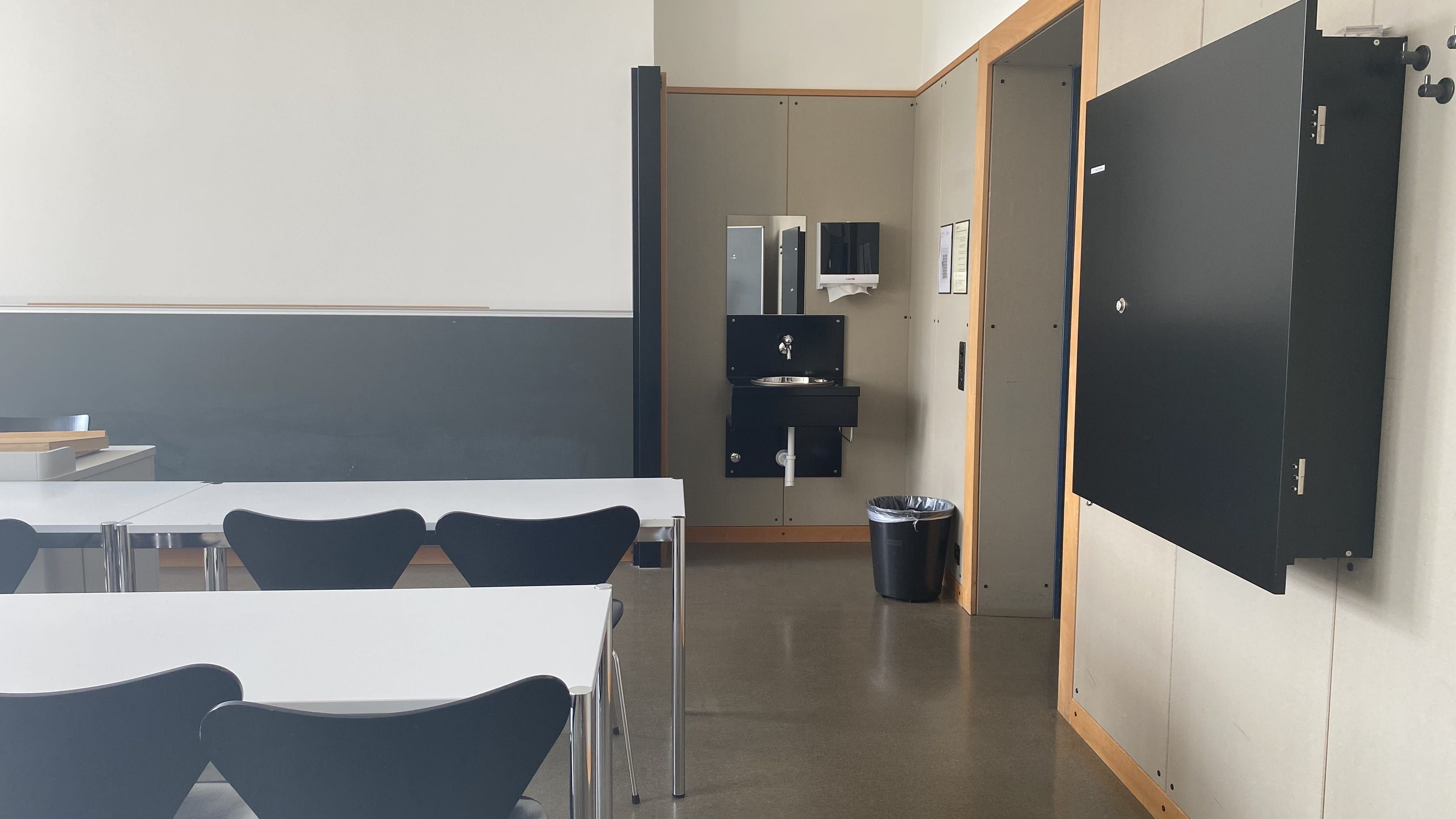 Seminarraum KOL-G-203: Ansicht auf den breiten Durchgang. Rechts neben der Eingangstür befindet sich ein Lavabo.