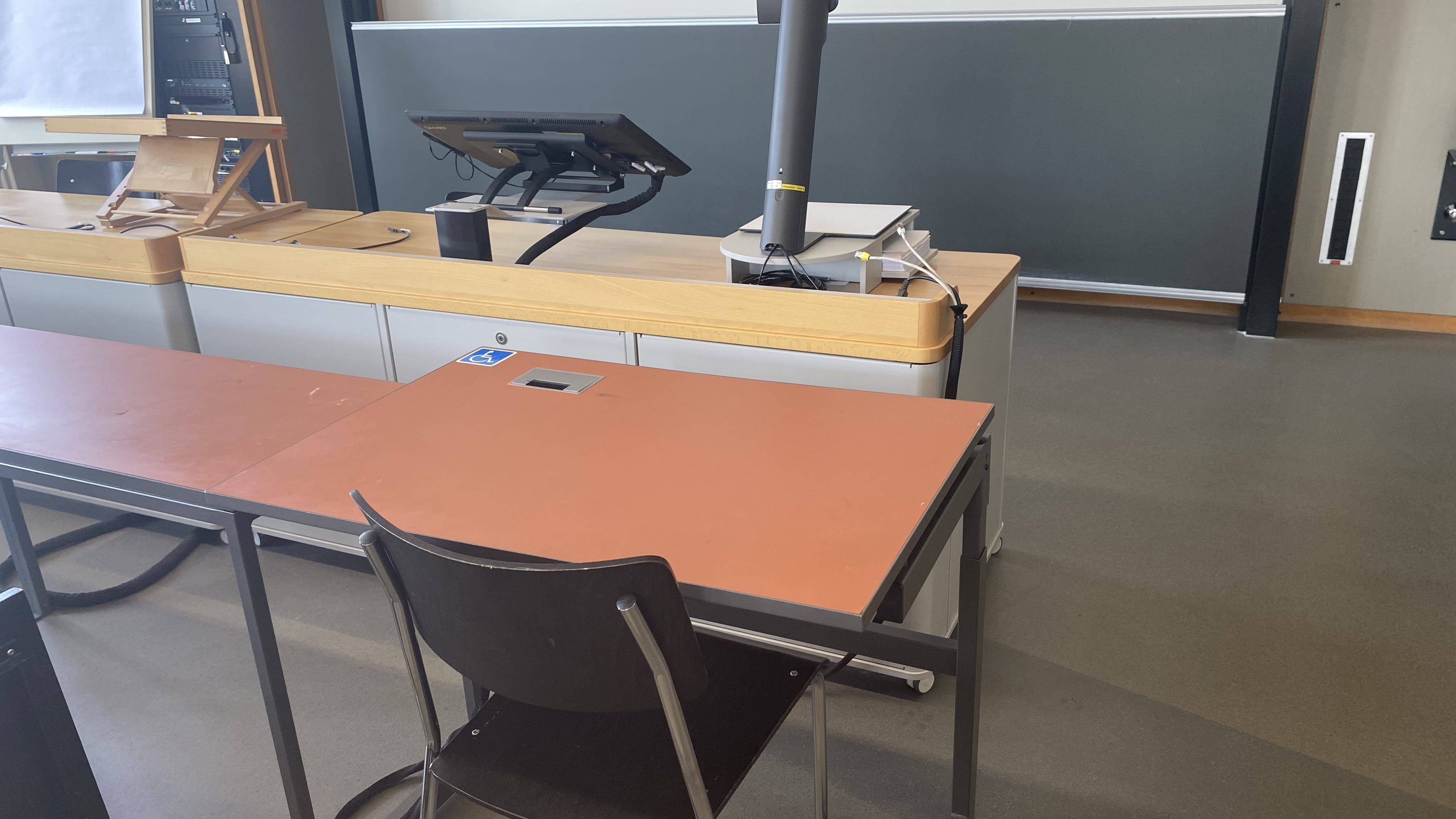 Hörsaal KOL-G-204: Ansicht auf den elektrisch höhenverstellbaren Tisch in der vordersten Reihe rechts, nahe der Eingangstür.