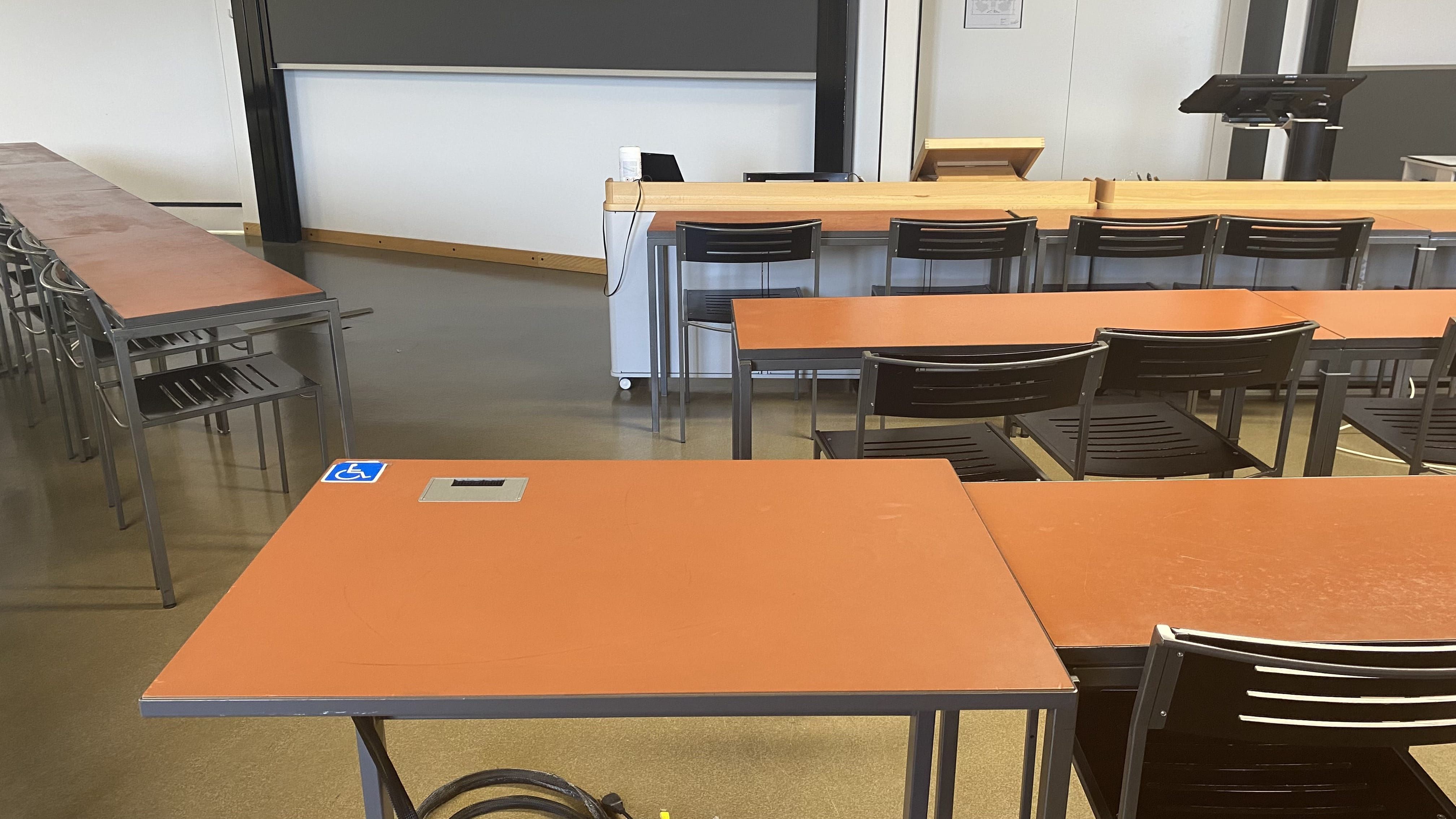 Hörsaal KOL-H-312b: Ansicht auf den elektrisch höhenverstellbaren Tisch mit Rollstuhl-Signet. Der Tisch befindet sich in der mittleren Sitzreihe in der dritten Reihe links.