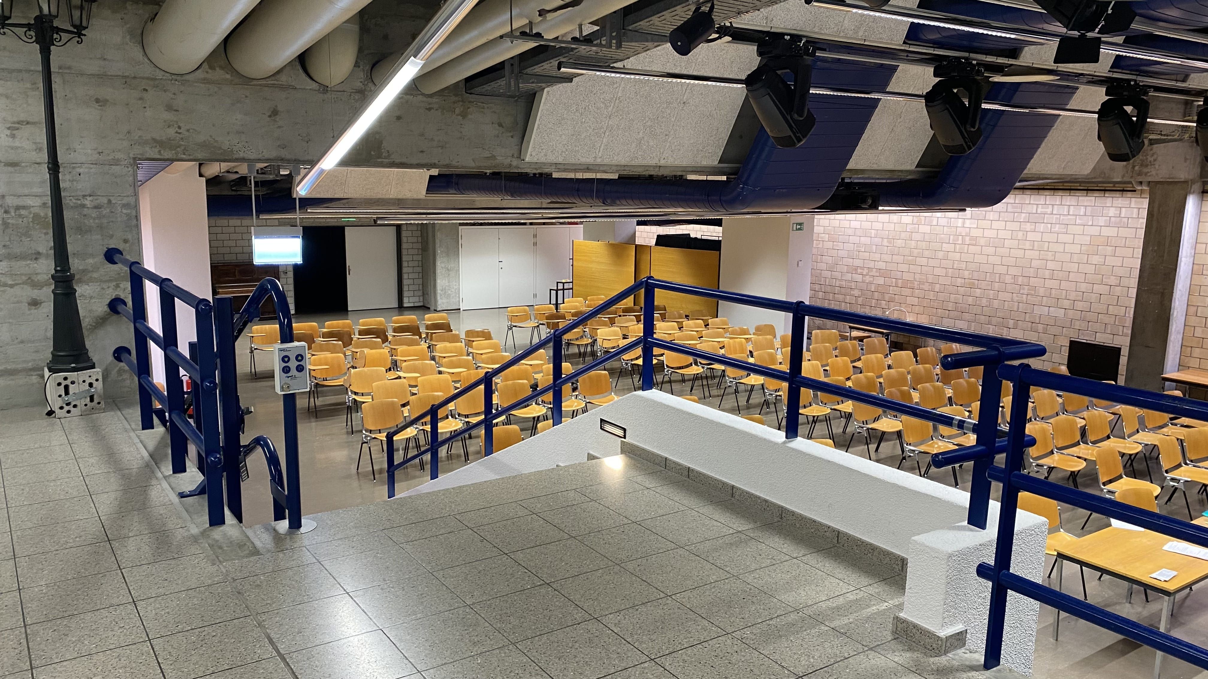 Aula Y21-F-65: Ansicht auf die Treppe, die in die Aula führt. Die Treppe verfügt über einen Treppenlift.