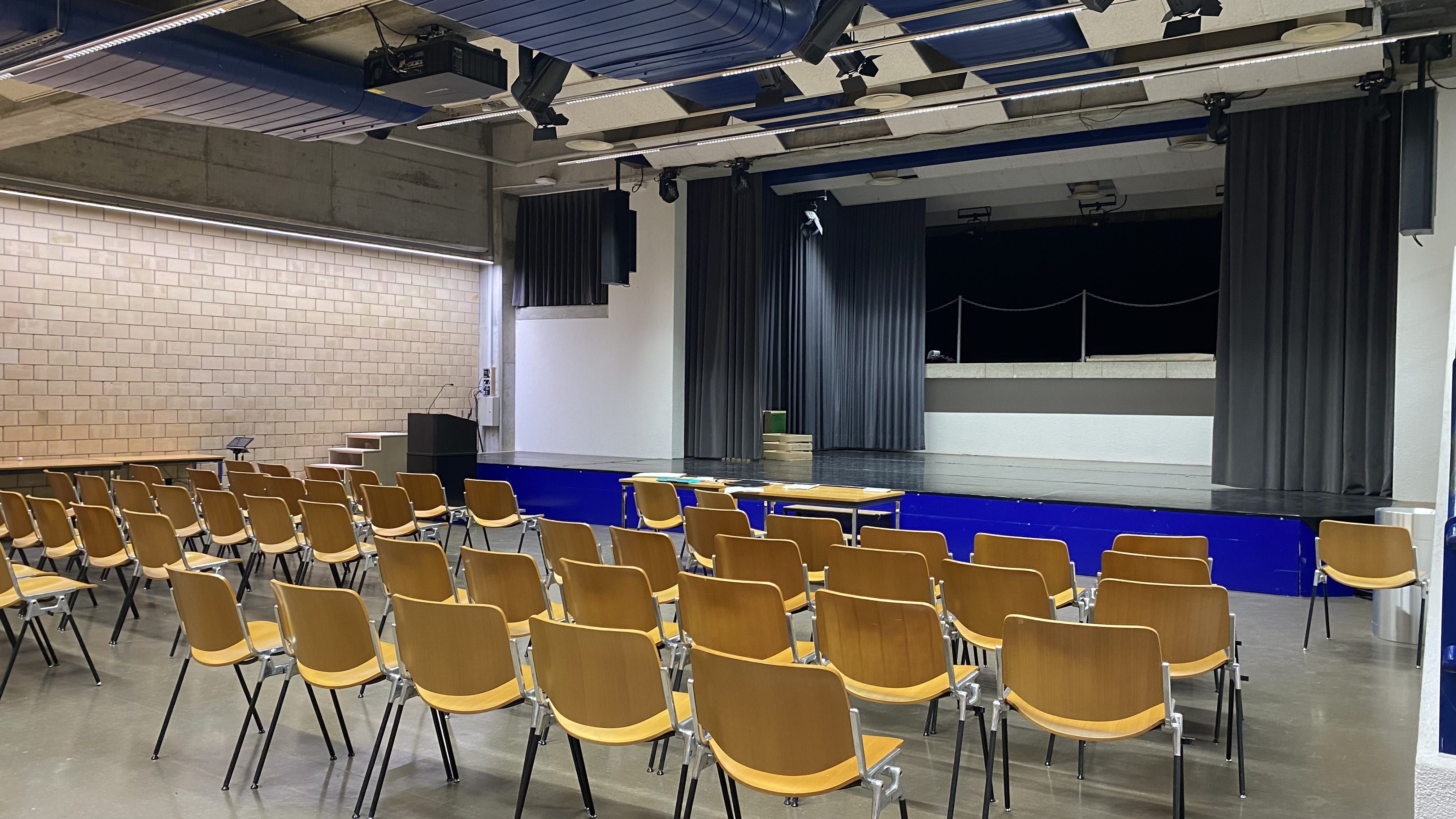 Aula Y21-F-65: Ansicht von den Sitzreihen aus zur Bühne hin.
