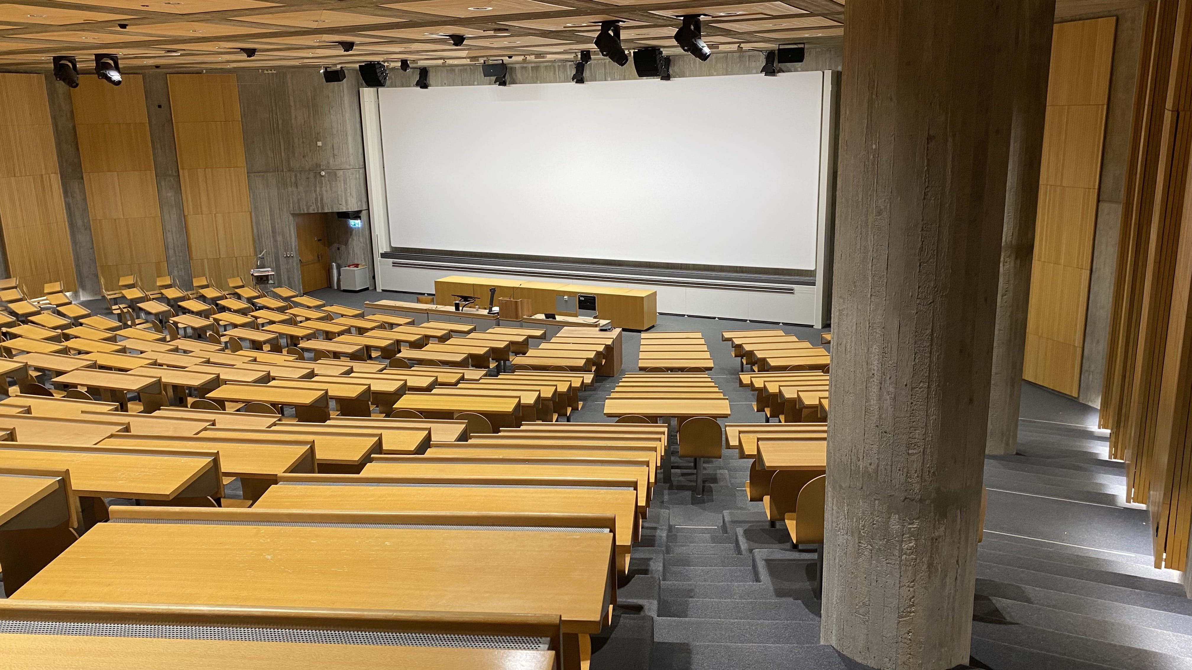 Hörsaal Y24-G-45: Ansicht auf den Raum von der rechten Eingangstür aus. Breite Stufen ganz links und rechts im Raum und schmale Stufen zwischen den Sitzreihen führen zum Dozierendenpult.