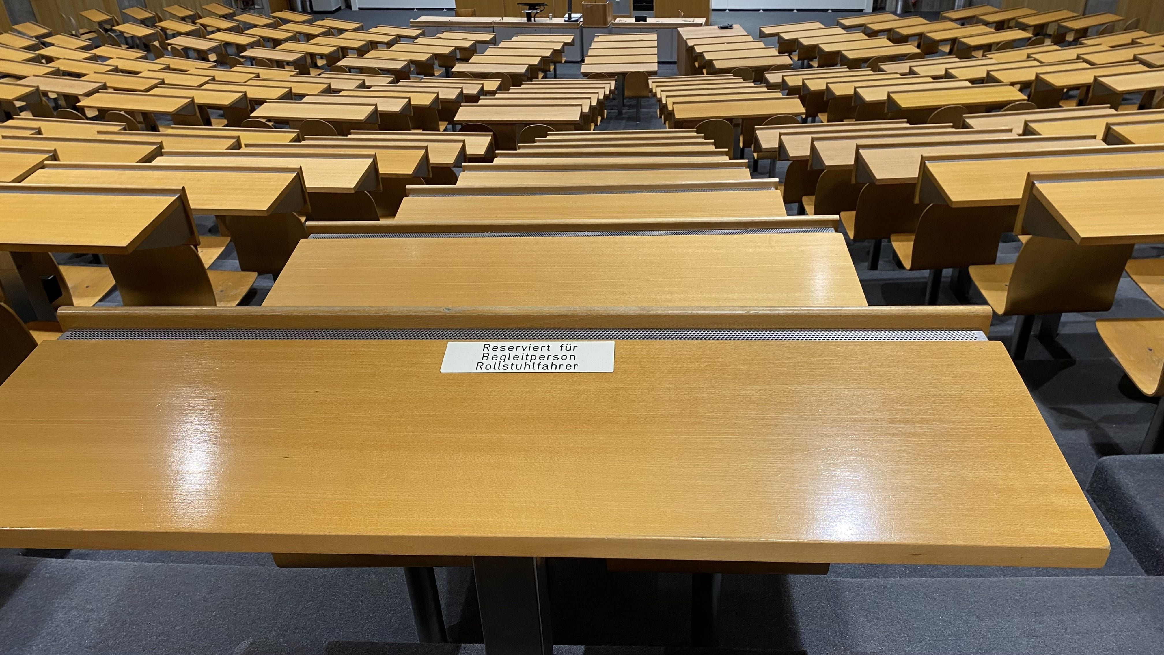 Hörsaal Y24-G-45: Ansicht auf den Tisch links vom Tisch mit Rollstuhl-Signet, der für Begleitpersonen von Rollstuhlfahrer:innen reserviert ist.
