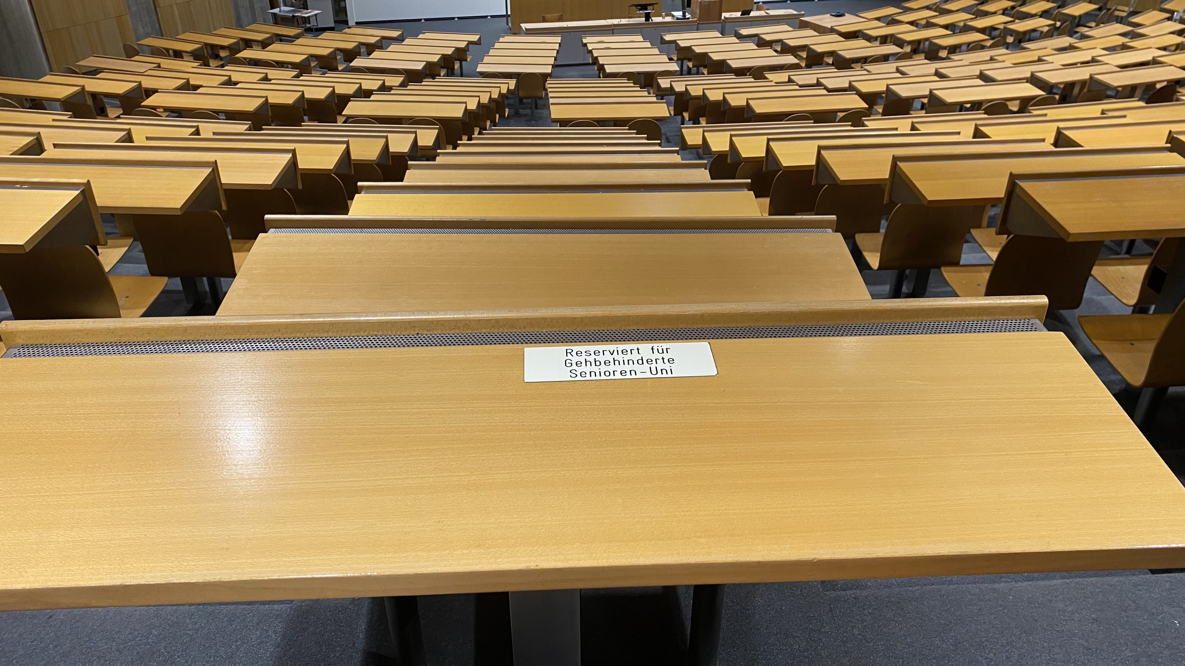 Hörsaal Y24-G-45: Ansicht auf einen Tisch links von der Mitte in der hintersten Reihe, der reserviert ist für gehbehinderte Personen der Senior:innen-Uni.