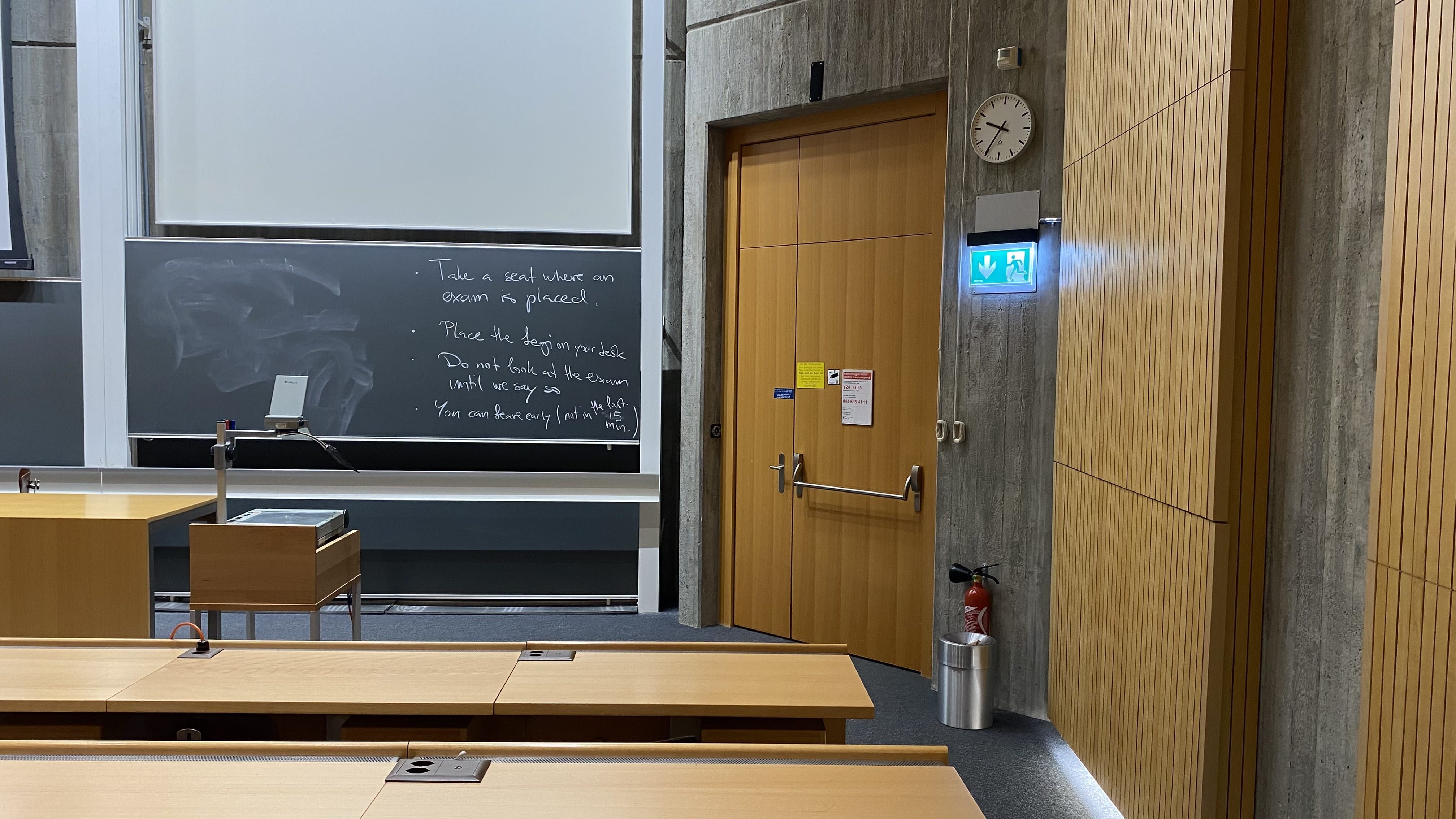 Hörsaal Y24-G-55: Ansicht auf die Eingangstür auf der unteren Ebene neben dem Dozierendenpult.