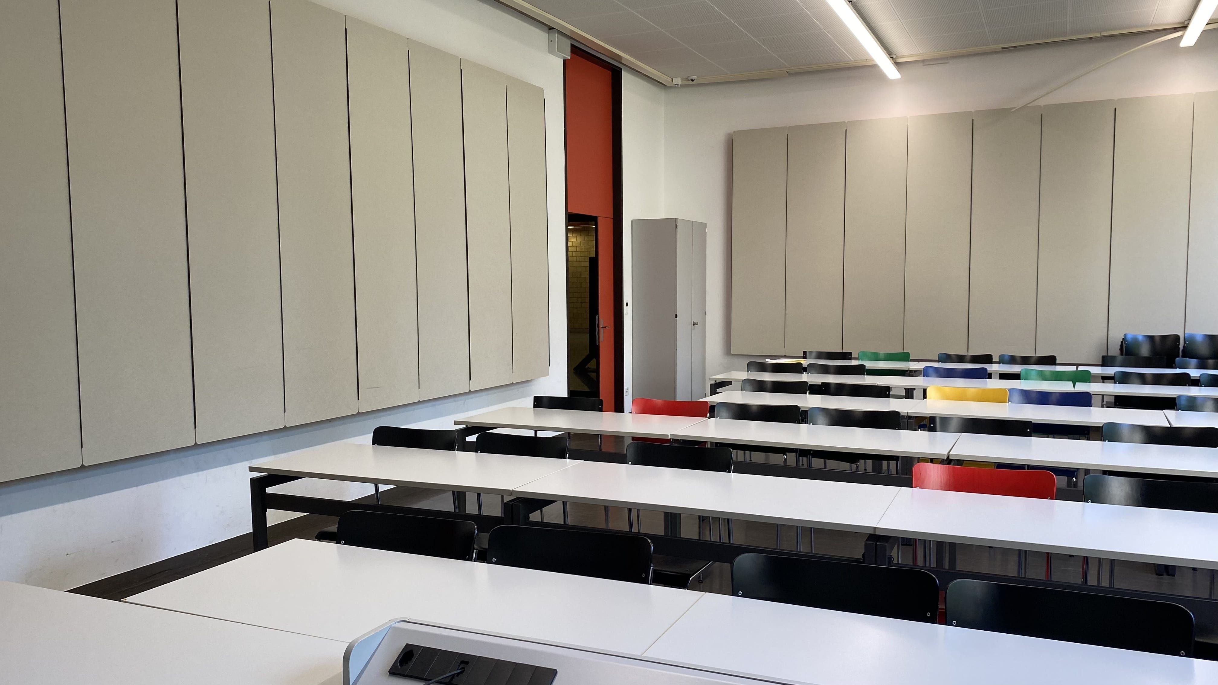 Seminarraum Y23-G-4: Ansicht auf den Raum vom Dozierendenpult aus. Die linke Eingangstür in rot befindet sich in der Mitte des Bildes.