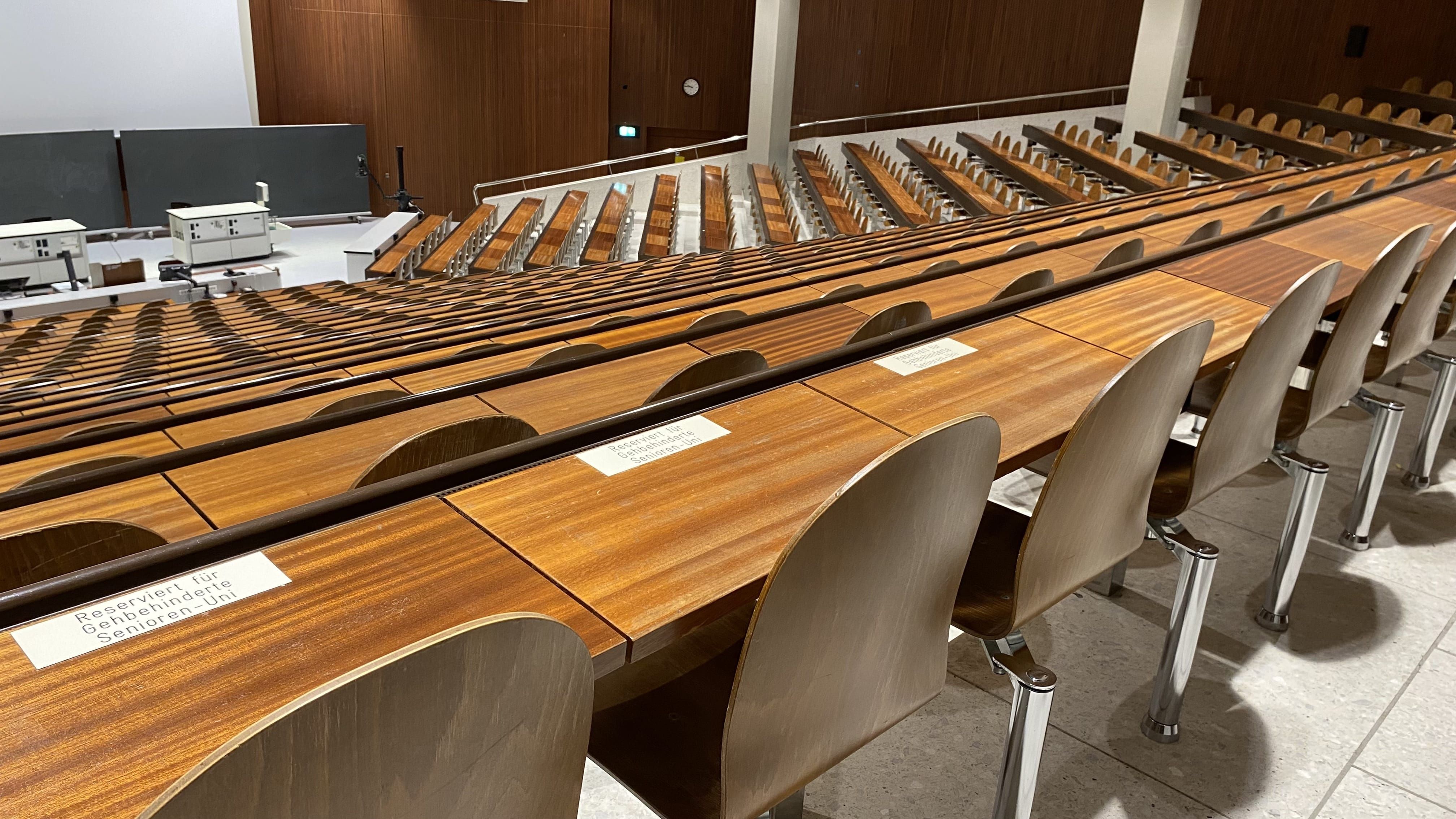 Hörsaal Y04-G-30: Ansicht auf drei Plätze die reserviert sind für Gehbehinderte Personen der Senioren-Uni. Die Plätze befinden sich in der hintersten Reihe in der mittleren Sitzreihe.